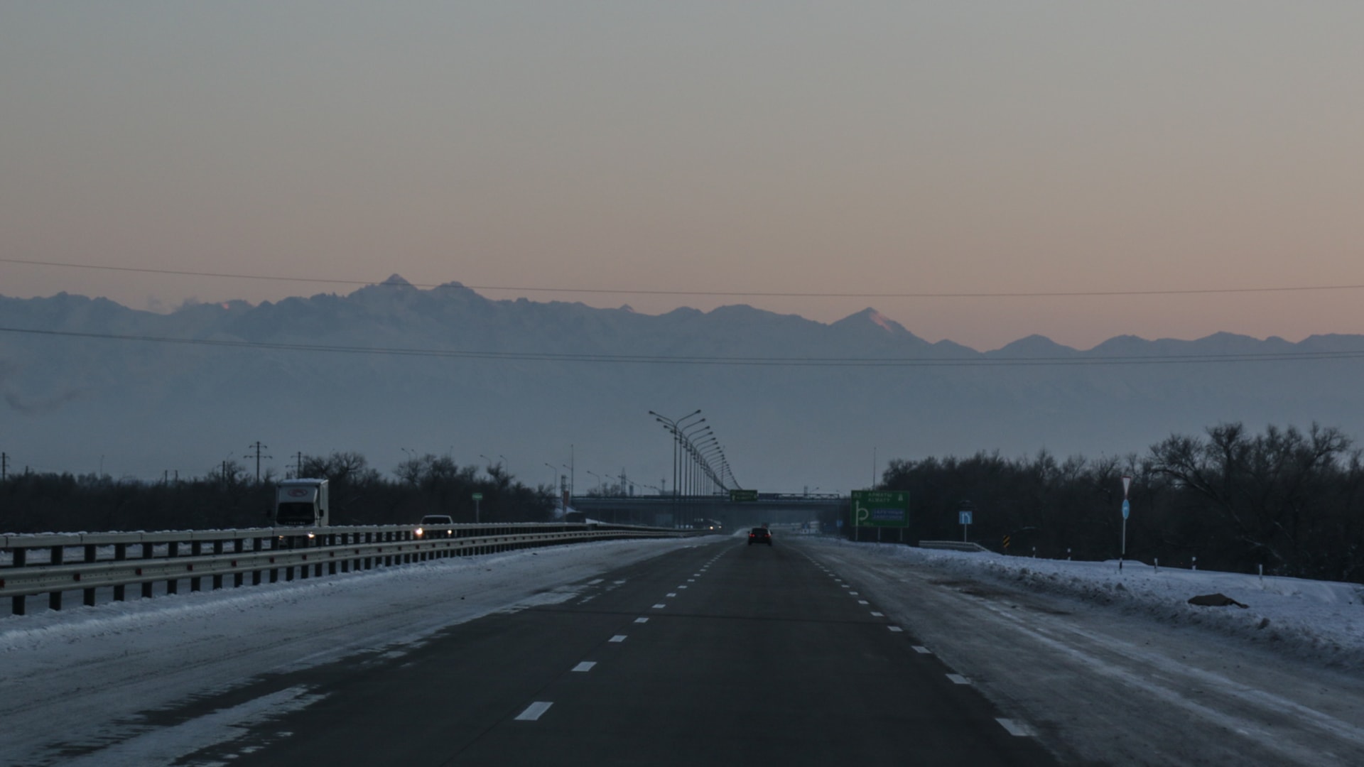Winterstraße bei Irkutsk mit kyrillischen Straßenschildern und schneebedeckten Bergketten im Morgenlicht.