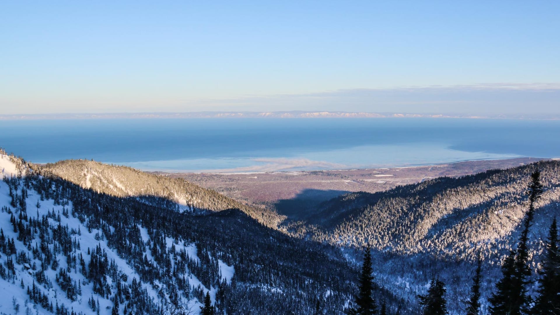 Skitour am Baikalsee: Panoramaaufnahme von verschneiten Nadelwäldern und dem tiefblauen Baikalsee im Hintergrund