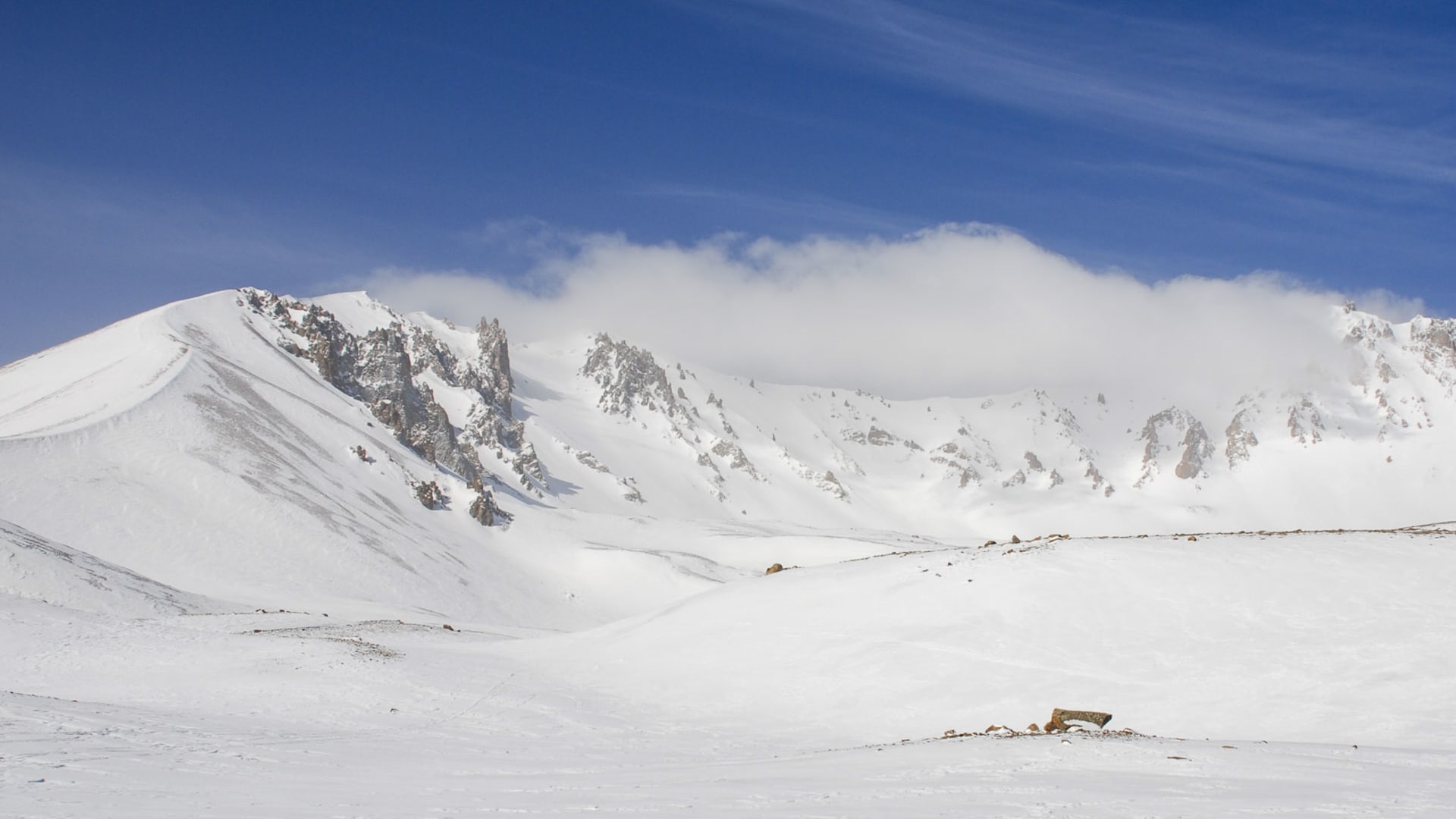 Weitläufiges Schneebecken mit felsigem Gebirgskamm im Taurusgebirge unter blauem Winterhimmel, keine Personen.