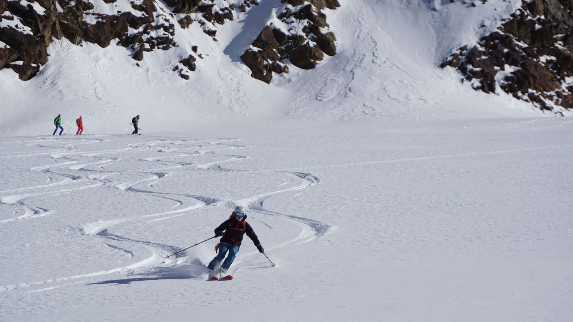 Skitourengeher in Schwungbewegung auf unberührtem Pulverschneehang im Ortlergebiet, drei weitere stehen im Mittelgrund.