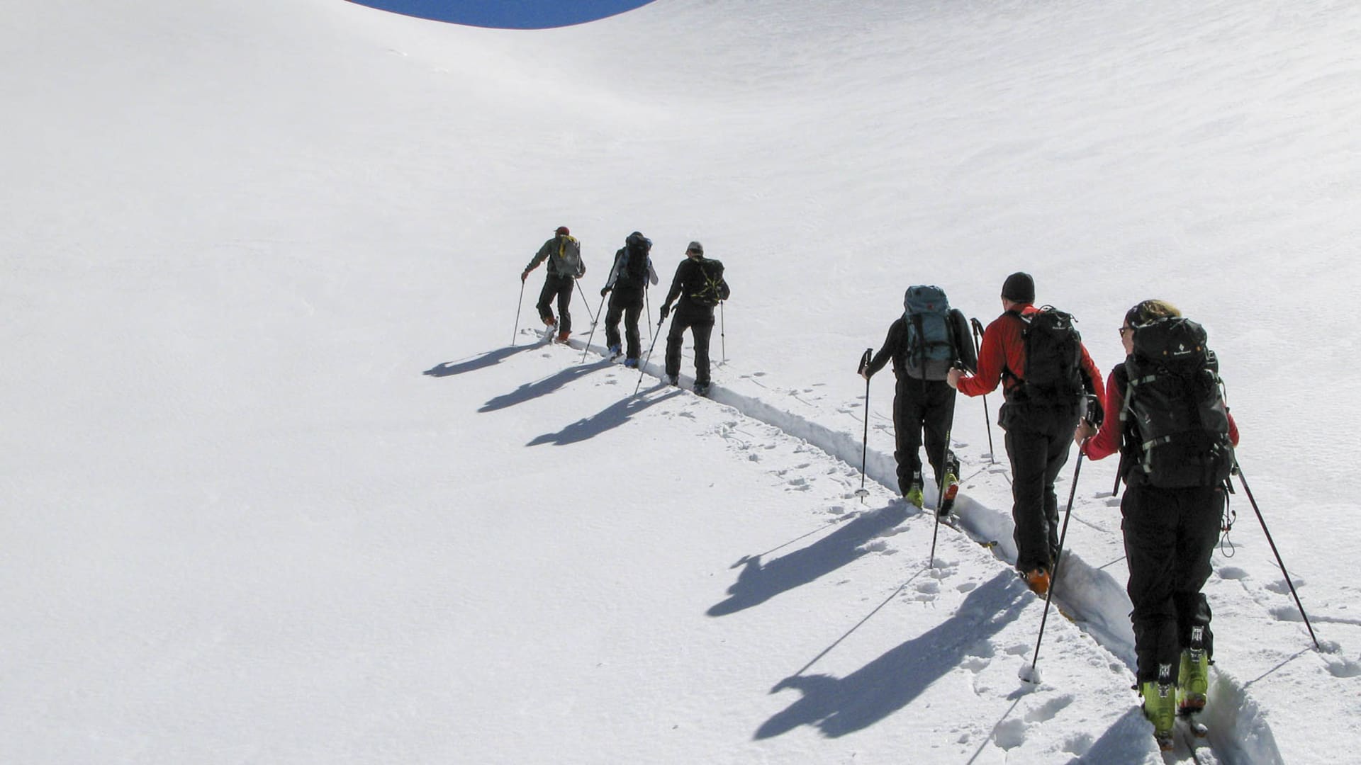 Fünf Skitourengeher steigen in Einspur mit Fellen und Skistöcken einen sonnenbeschienenen Schneehang im Taurus auf.
