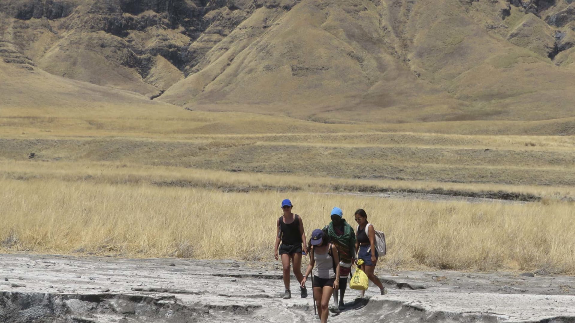 Vier Trekker wandern über helle Gesteinsformation auf der trockenen Hochebene im Ngorongoro-Gebiet Tansanias.