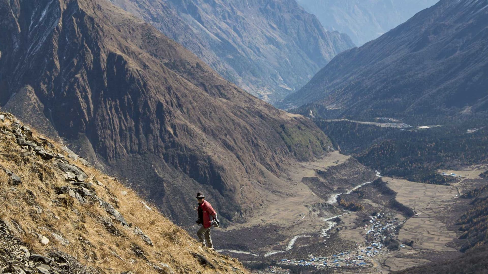 Trekking am Manaslu: ein Trekker in roter Jacke steht auf einem Grashang und blickt auf das Hochgebirgstal bei Samagon in Nepal.