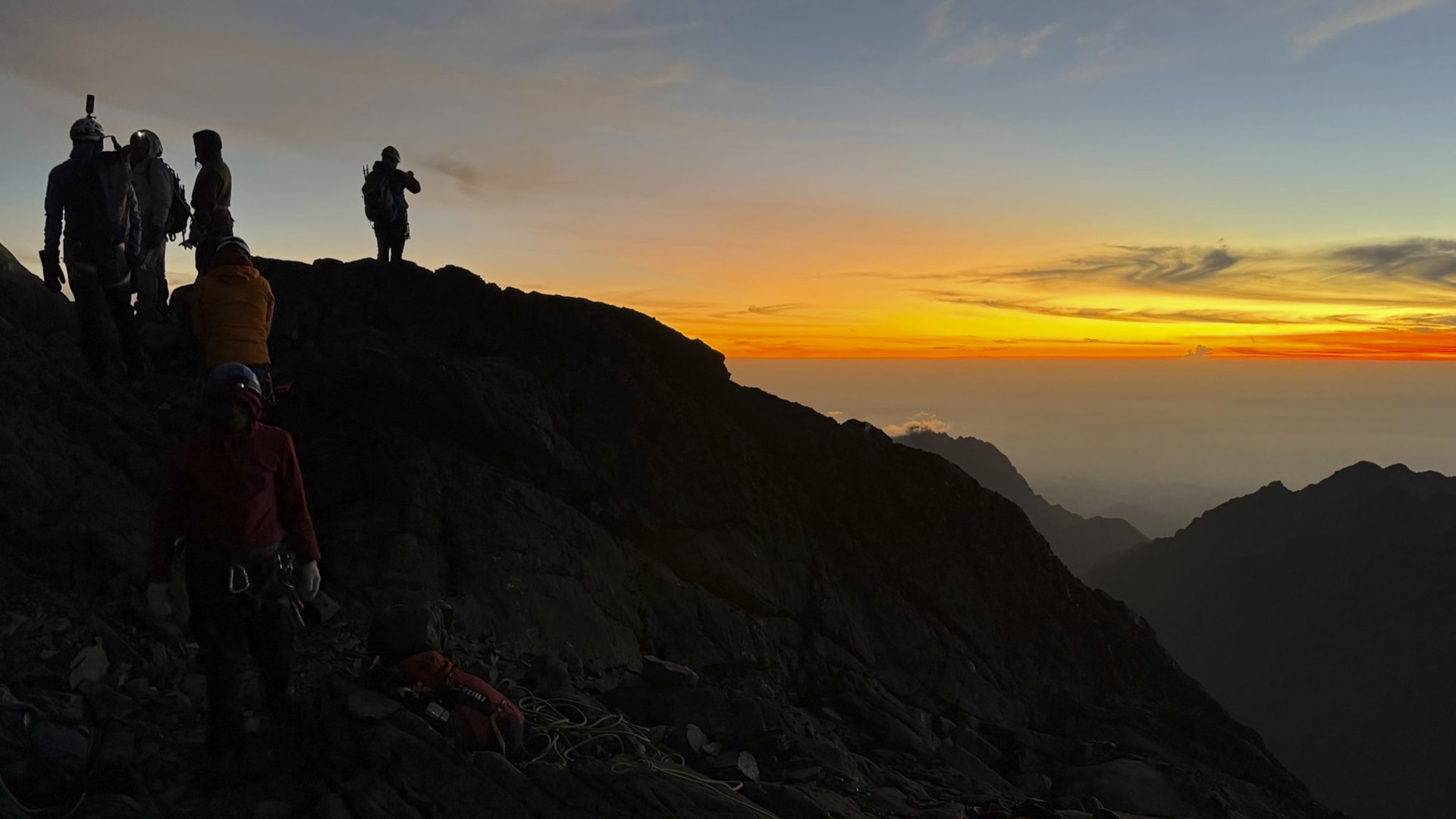 Trekking im Ruwenzori Gebirge: fünf Trekker als Silhouetten auf felsigem Grat beim Sonnenaufgang.