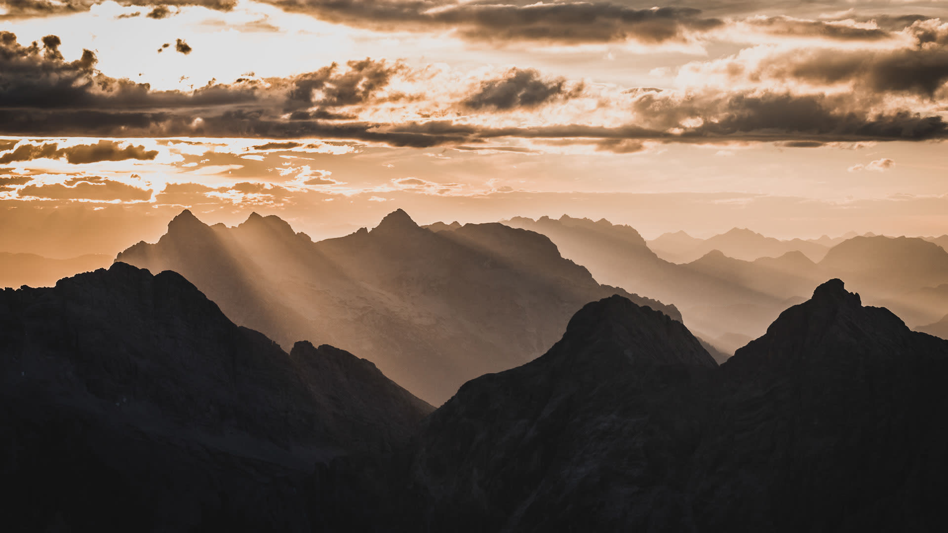 Bergwanderung am Watzmann: Panorama gestaffelter Bergketten bei Sonnenuntergang mit Krepuskularstrahlen.