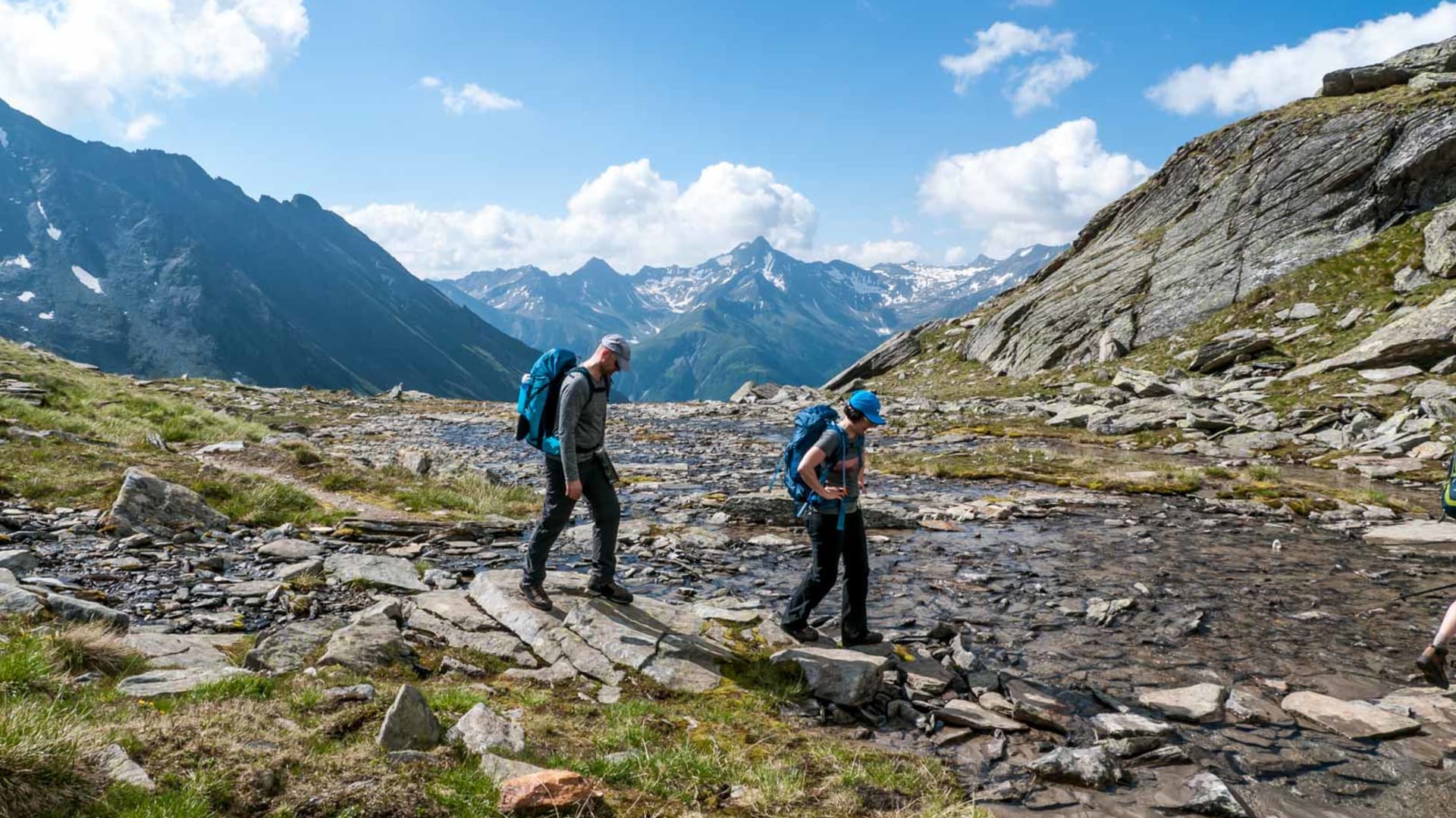 Hohe Tauern Bergwanderung: zwei Bergwanderer mit Trekkingrucksäcken überqueren einen flachen Gebirgsbach auf einem Hochplateau.
