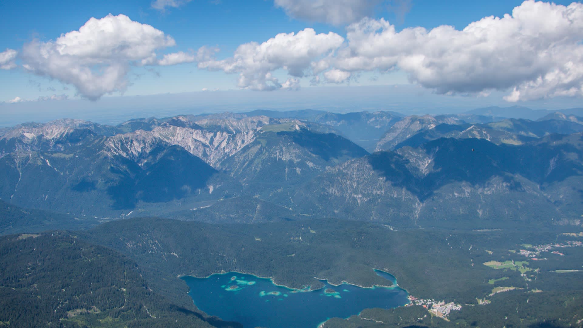 Bergwanderung an der Zugspitze: Vogelperspektive auf den türkisblauen Eibsee mit Nadelwäldern und Bergkette.