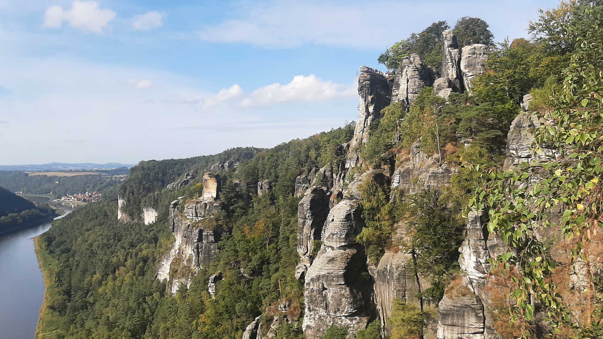 Bergwanderung Sächsische Schweiz: Sandsteinfelsnadeln überragen ein Flusstal mit Ortschaft und bewaldeten Hügeln.