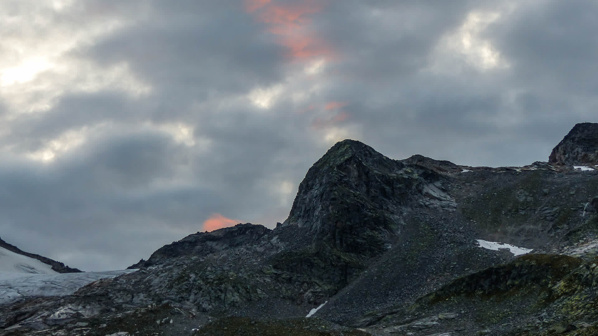 Bergwanderung in den Hohen Tauern: Felsgipfel mit Firnfeld und bewölktem Abendhimmel in rötlich-orangen Tönen.
