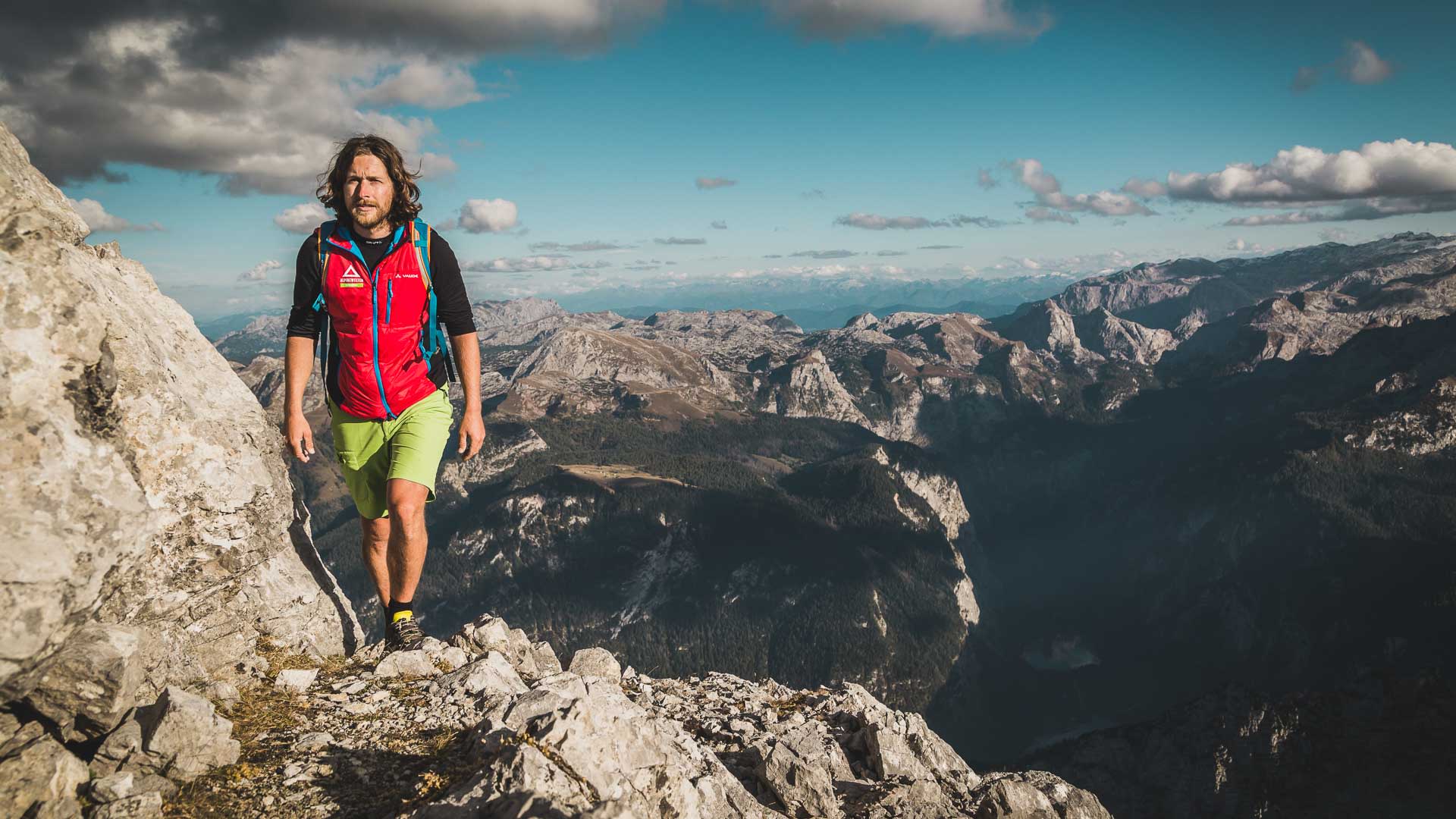 Ein Bergwanderer traversiert einen felsigen Kalksteingrat in den Berchtesgadener Alpen mit alpinem Panorama im Hintergrund.