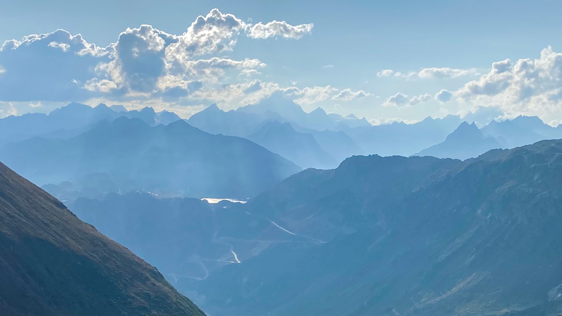 Bergwanderung am Furkapass mit Panorama auf das Finsteraarhorn und gestaffelte Gebirgsketten im bläulichen Dunst.