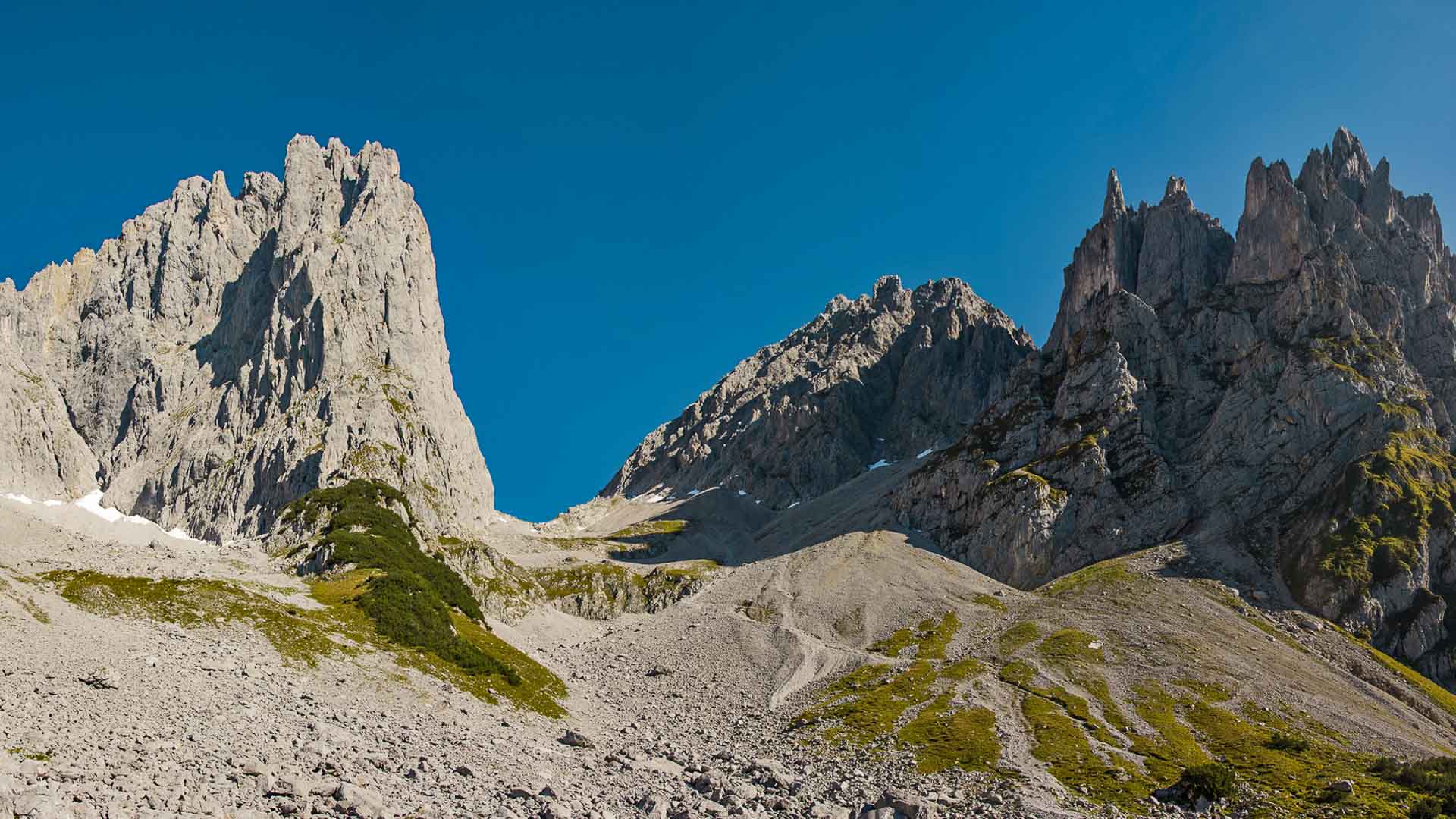 Bergwanderung auf der Kaiserkrone im Wilden Kaiser: Schuttfeld aus Kalkstein-Geröll mit Pfad vor markanten Felstürmen im Sommer.
