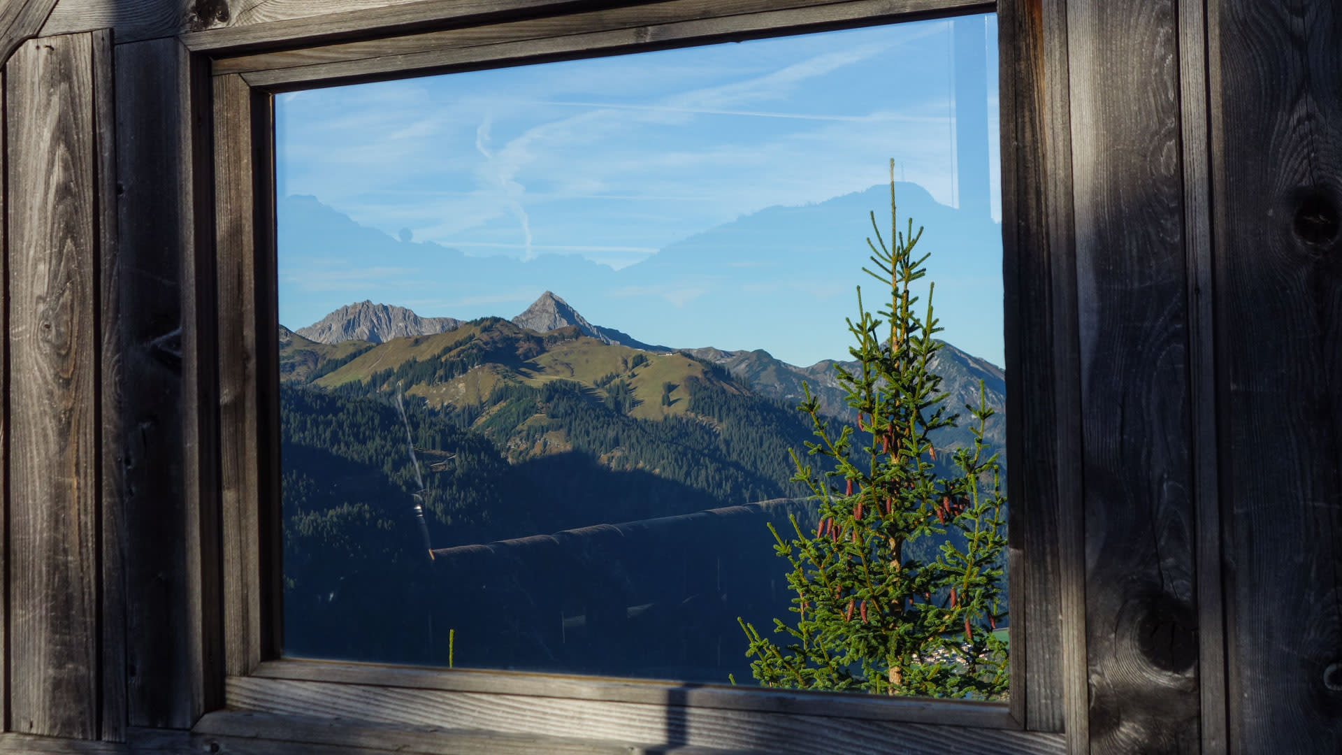 Bergwanderung im Tannheimer Tal: Blick durch Holzfenster des Gimpelhauses auf Almhänge und felsige Gipfel.