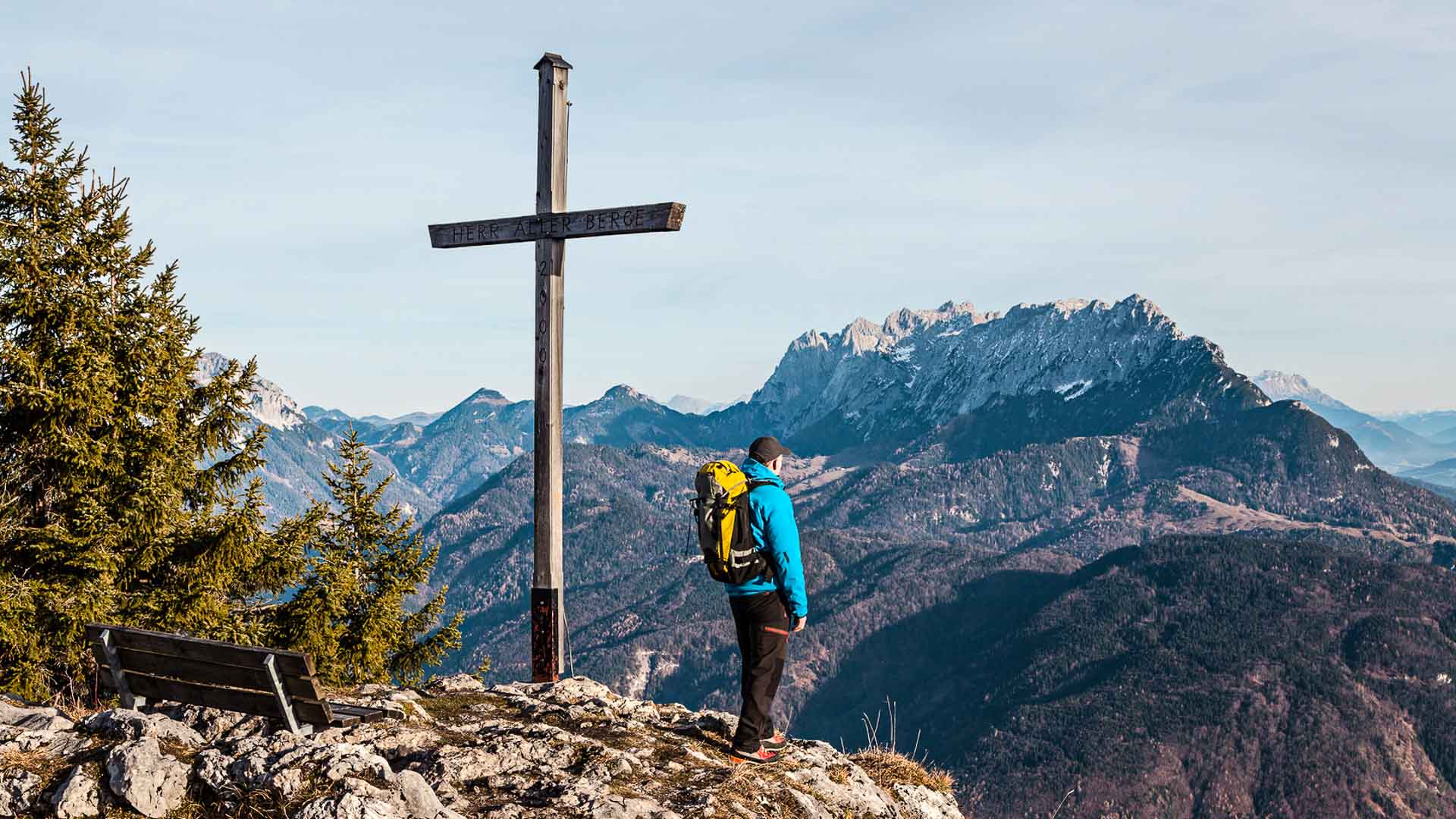 Bergwanderer steht am Gipfelkreuz mit Inschrift HERR ALLER BERGE bei der Bergwanderung im Wilden Kaiser.