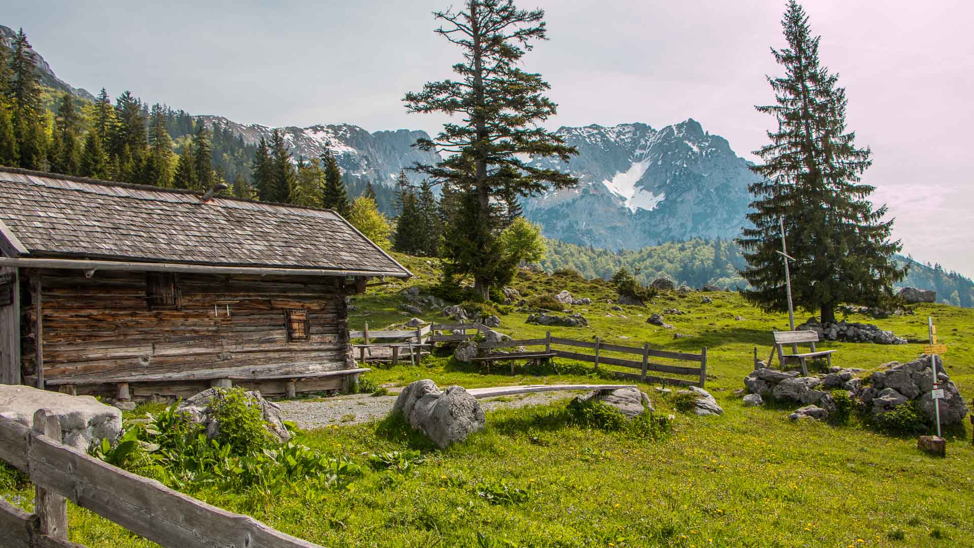 Bergwanderung im Wilden Kaiser: alte Holzhütte auf der Alm mit Kalkfelswänden und Schneefeldern im Hintergrund.