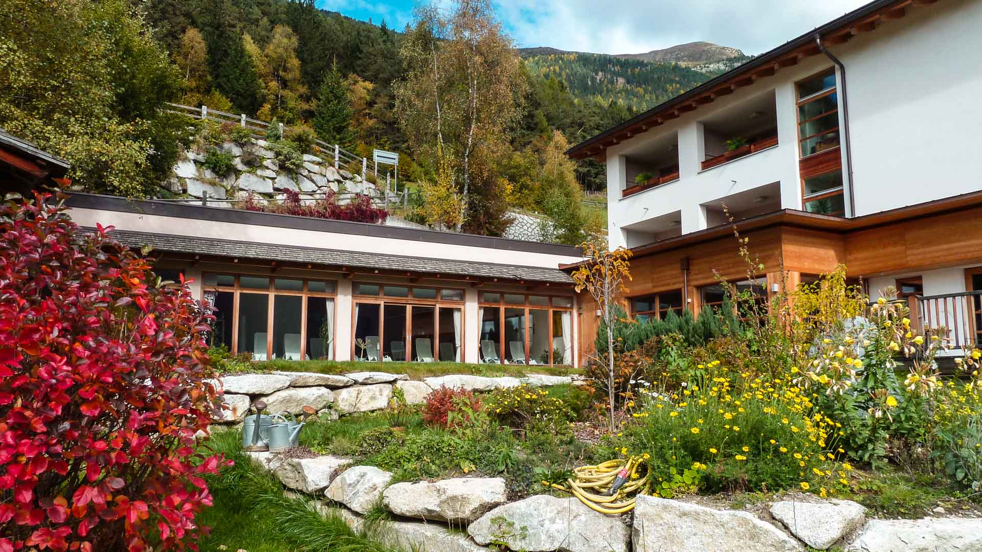 Bergwanderung ab Hotel Mossmaier in Südtirol: Gebäude mit Glasfront und Holzfassade in herbstlichem Garten