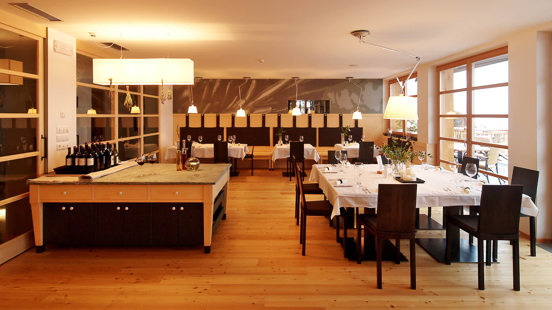 Restaurantraum eines Hotels in Südtirol mit gedeckten Tischen, Weinflaschen und Blick auf verschneites Balkongeländer.