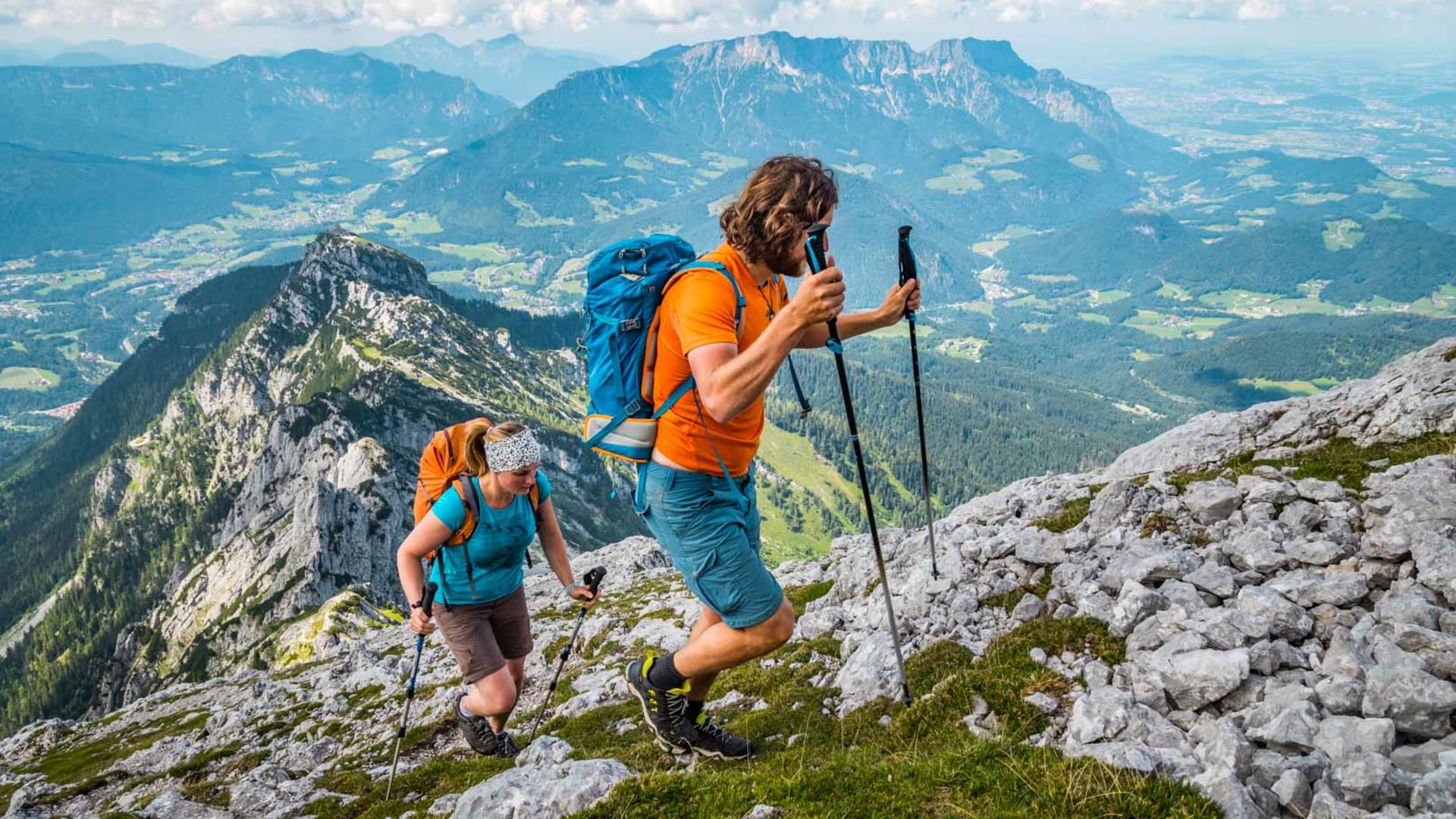 Zwei Bergwanderer steigen mit Wanderstöcken über einen steilen Kalkgrat in den Berchtesgadener Alpen