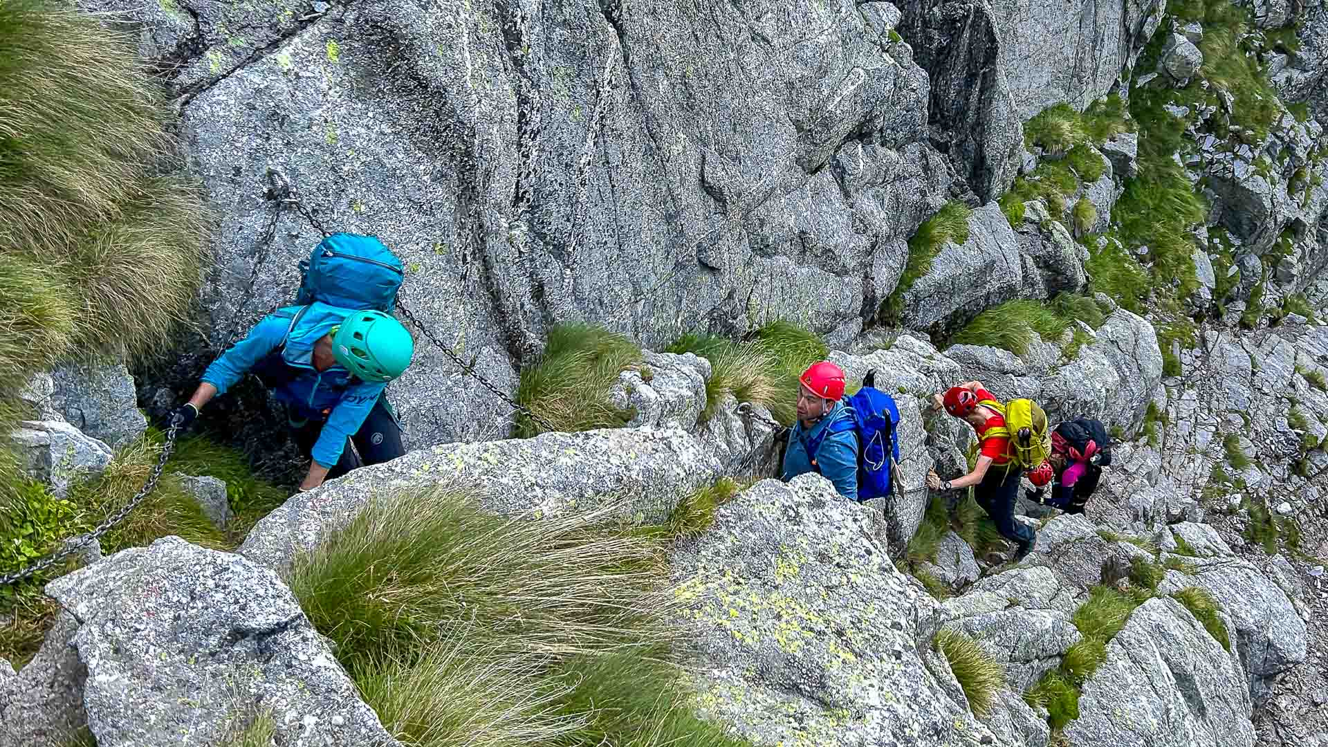 Bergwanderung im Bergell: Vier Bergwanderer steigen mit Eisenkette gesichert eine Granitfelstufe am Sentiero Roma auf.
