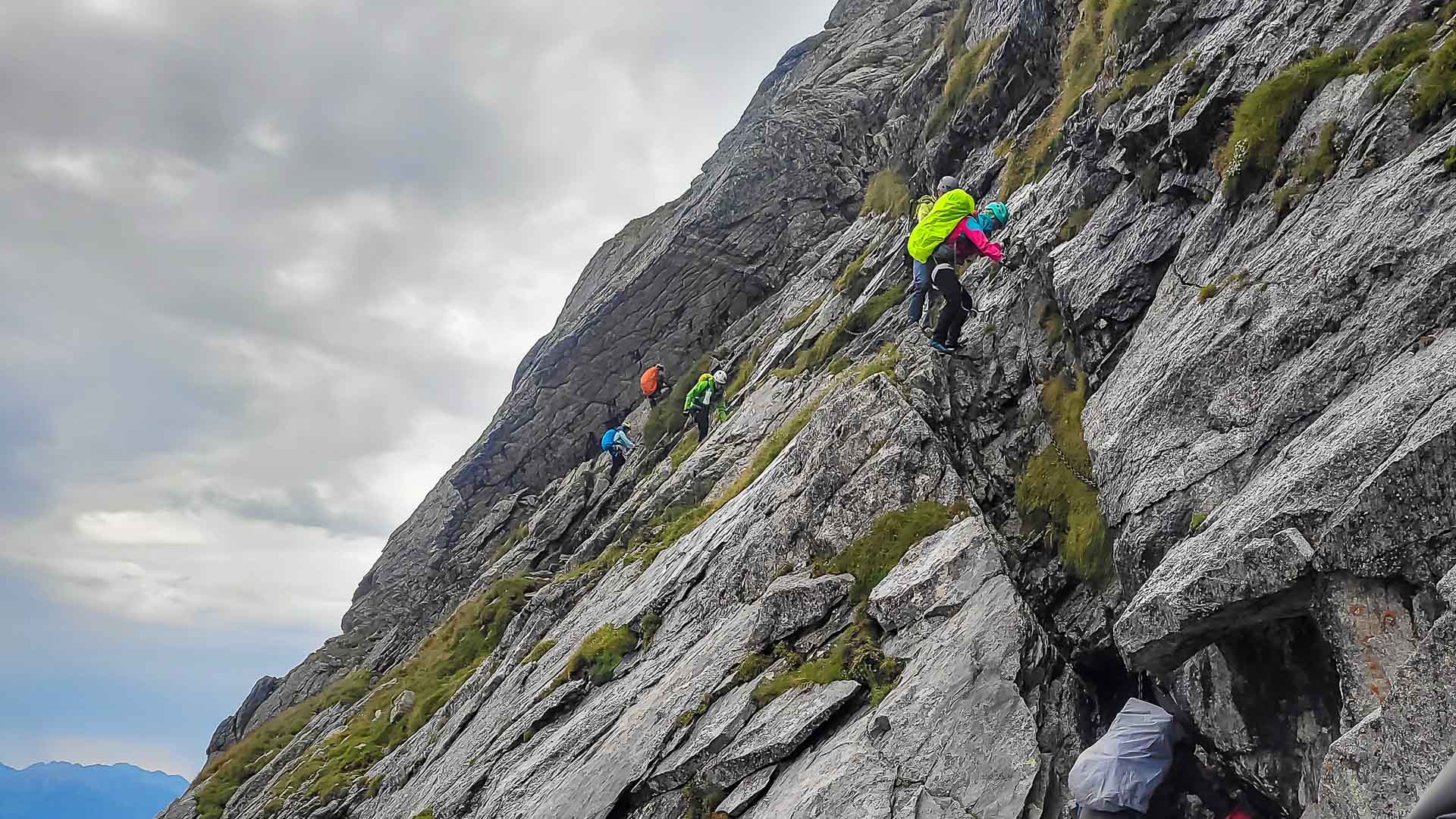 Gruppe von fünf Bergwanderern klettert mit Kettengeländer an einer Felswand am Sentiero Roma im Bergell aufwärts.