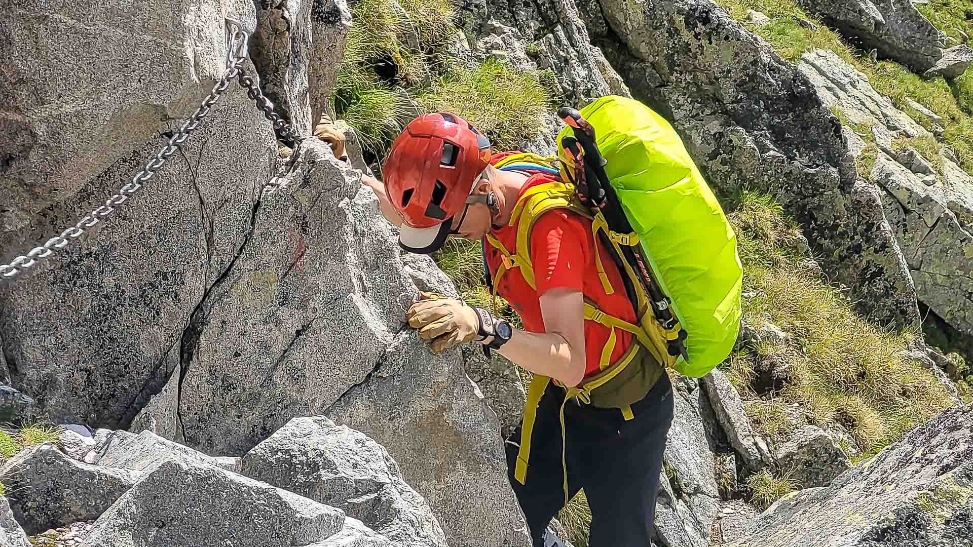Bergwanderer mit Helm und Rucksack klettert an gesicherter Granitfels-Passage mit Kette im Bergell.