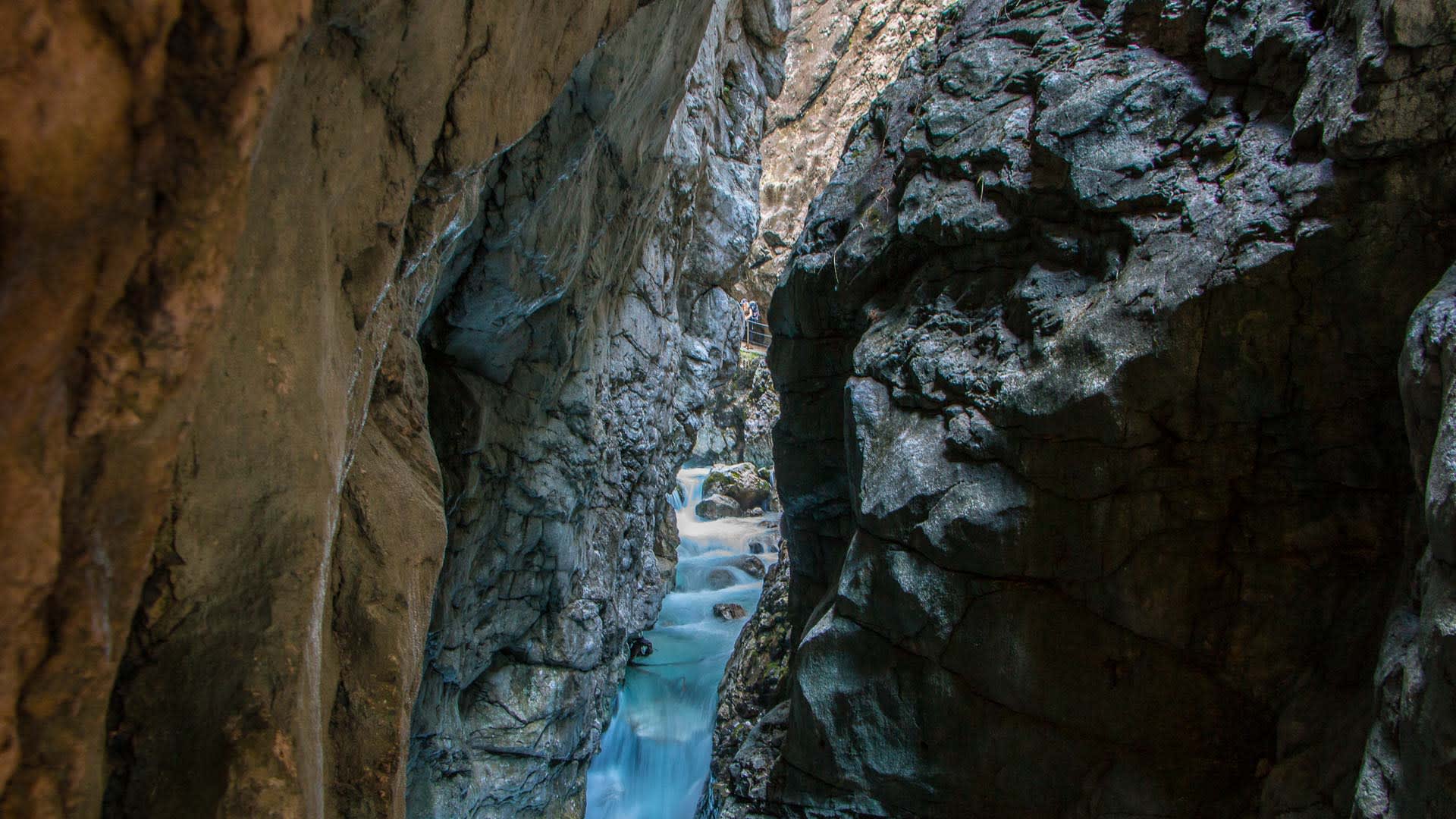 Bergwanderung durch die Partnachklamm: enge Felsschlucht mit türkisblauem Bach, Bergwanderer auf dem Steg am Felsen.