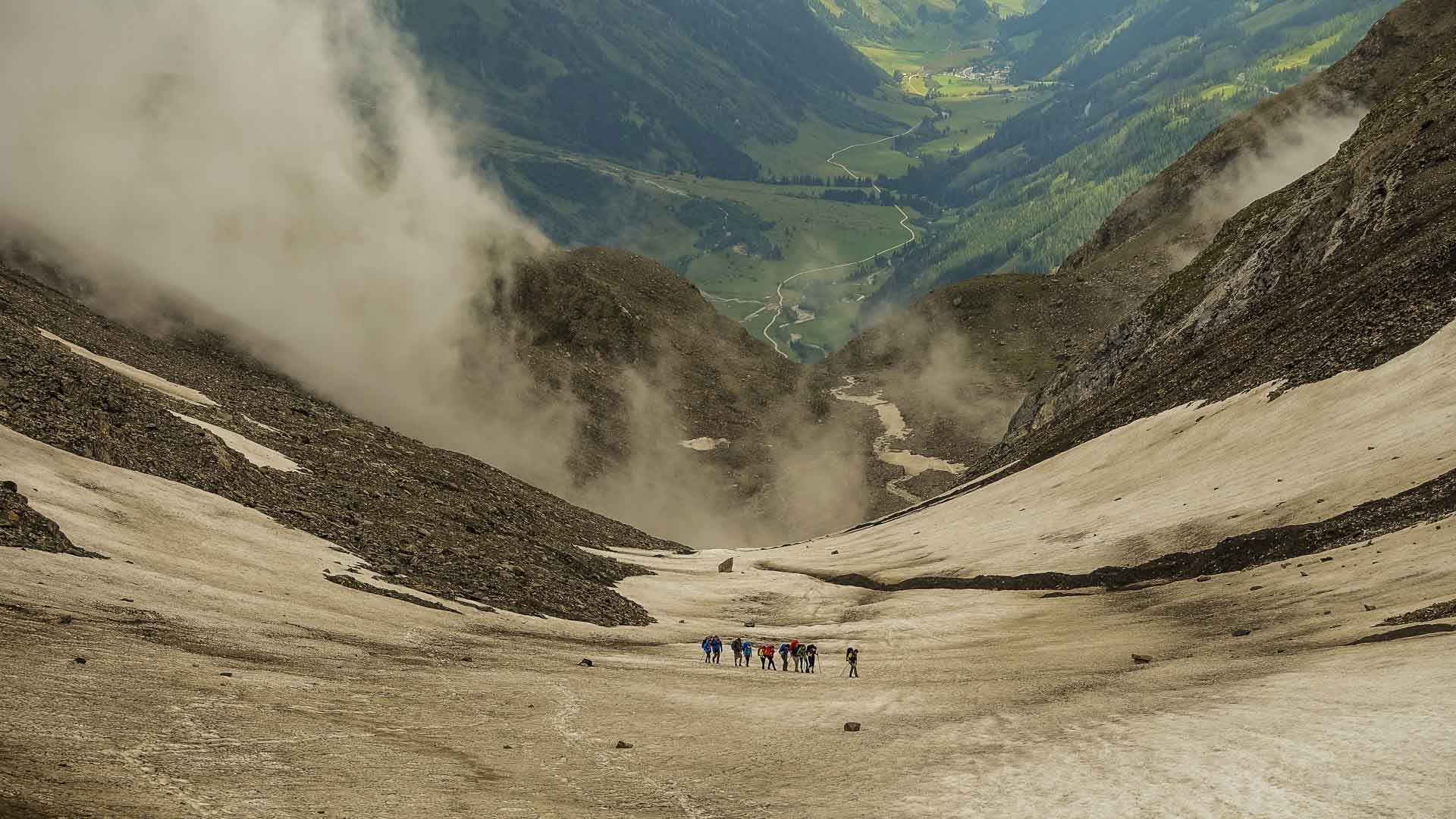 Bergwanderergruppe auf weitläufigem Schneefeld beim Abstieg in ein Alpental auf der Alpenüberquerung.
