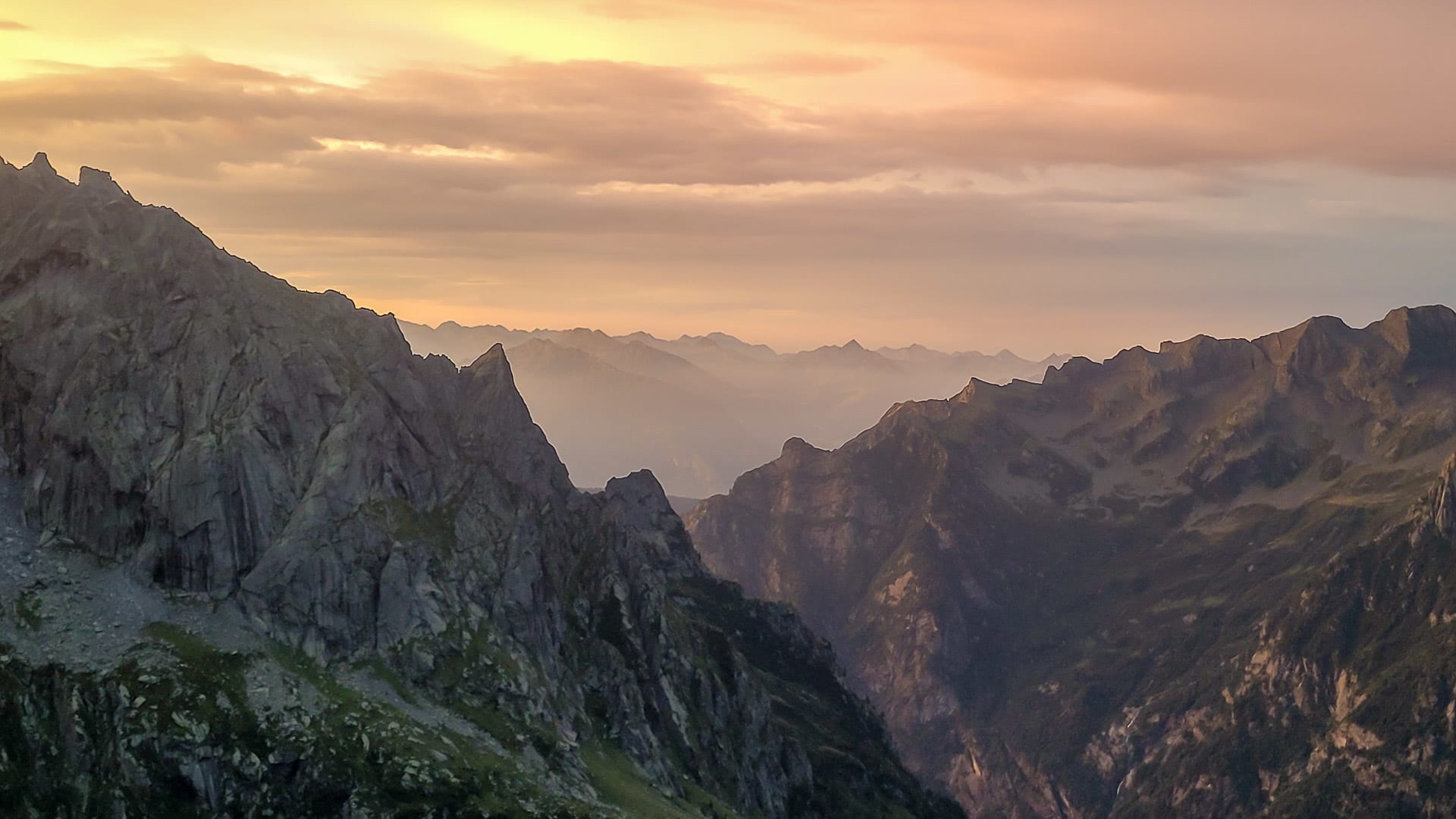 Bergwanderung im Bergell: Panoramablick auf tief eingeschnittenes Tal mit Abendrot und Wolkenschichten.