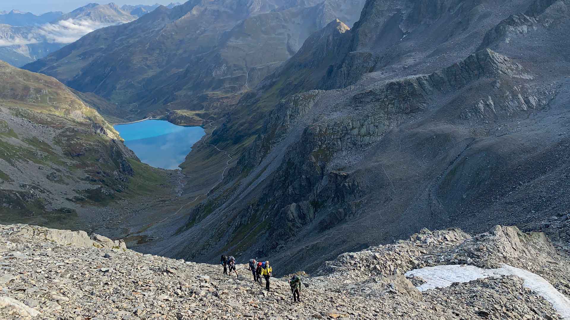Bergwanderergruppe steigt auf Steilhang auf, im Tal türkisblauer Stausee der Verwallgruppe, Ostalpen im Sommer.