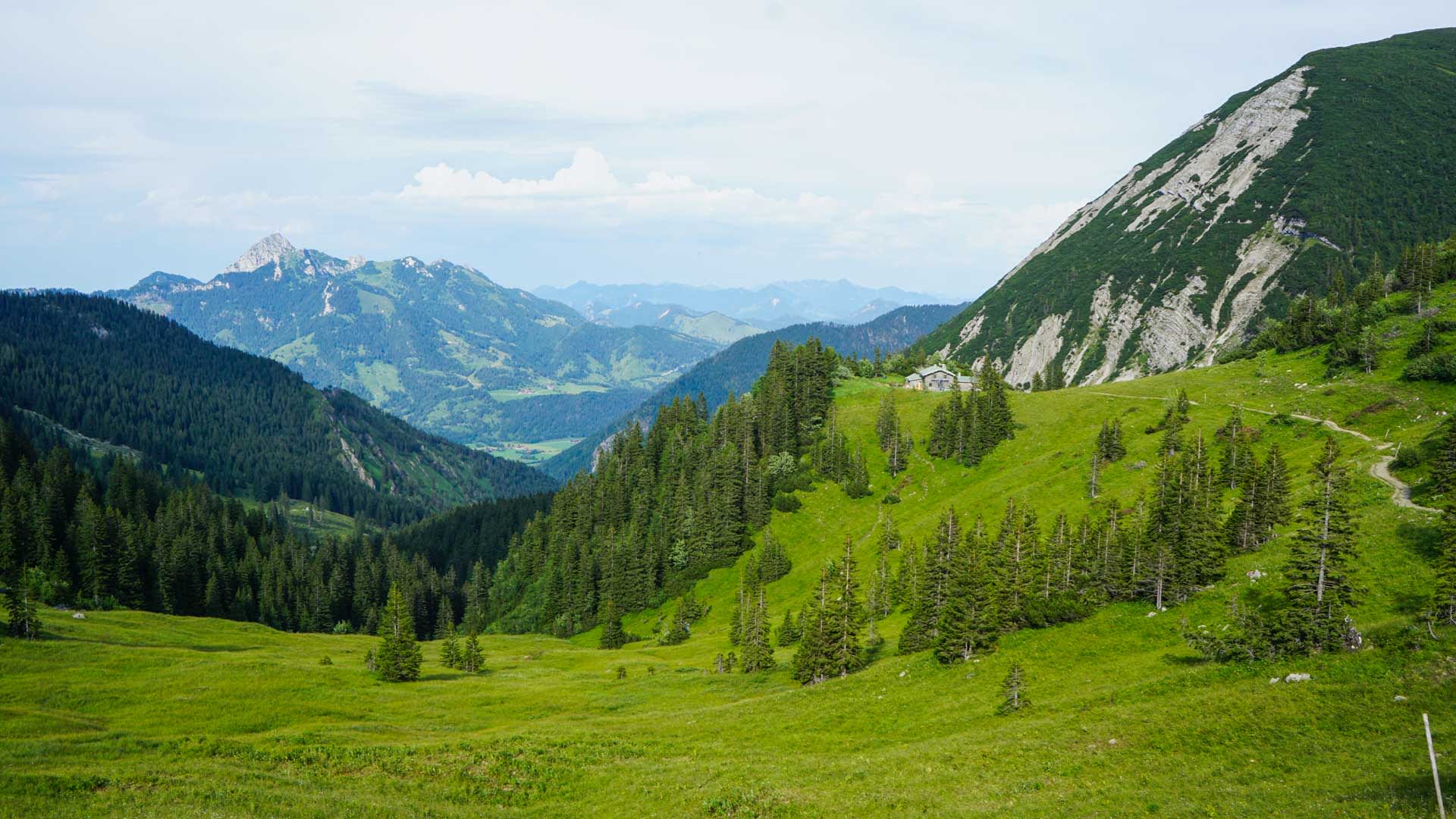 Bergwanderung Spitzingsee: Almwiese mit Almhütte, Kalkfelsgrat und weitem Talblick Richtung Tegernsee im Sommer.