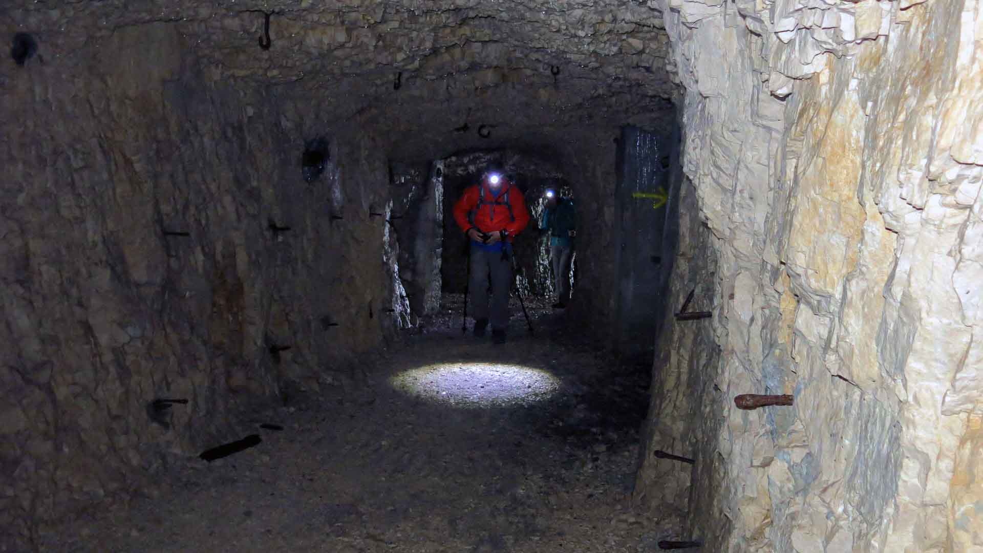 Zwei Bergwanderer mit Stirnlampen und Rucksäcken durchqueren den Kriegsstollen am Dente Italiano auf dem Friedensweg.