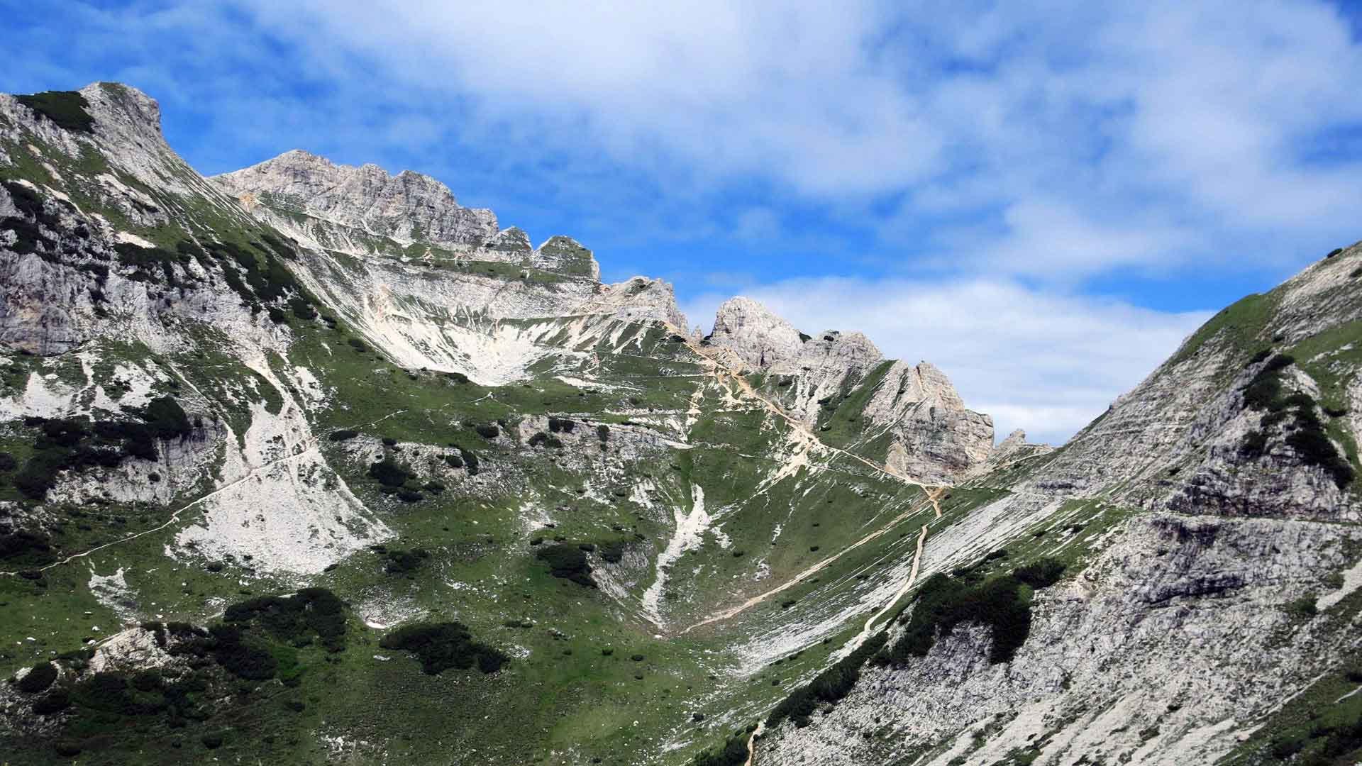 Bergwanderung zur Cima Carega: schmaler Wanderweg durch Kalkstein-Hang mit gezacktem Felskamm im Hintergrund.