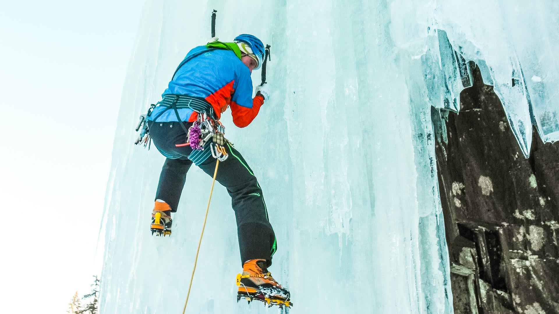 Eiskletterer mit Steigeisen und Eispickeln klettert in Froschperspektive an senkrechter Eiswand in Rjukan.