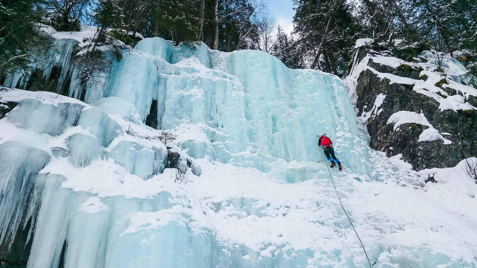Eiskletterer steigt mit Pickel und Steigeisen an blau-türkiser Eiswand im Maltatal auf.