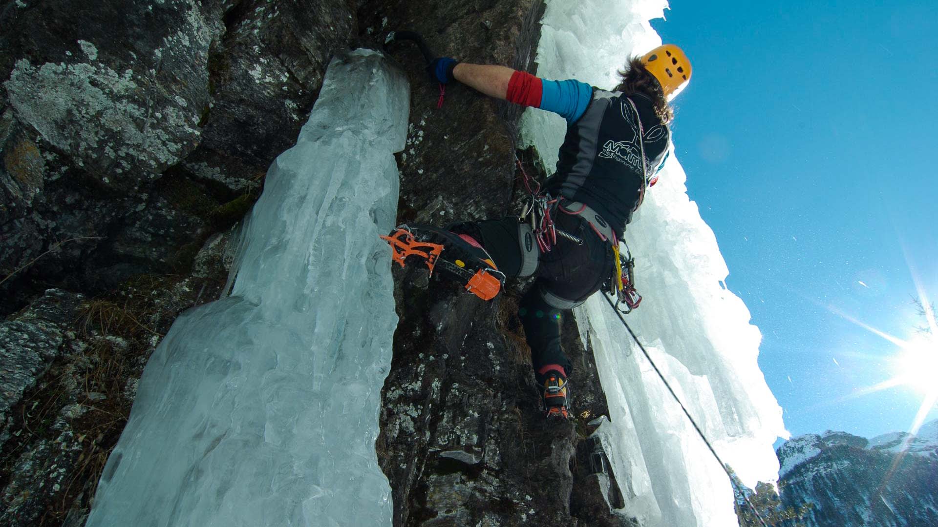 Eiskletterer steigt mit Steigeisen an einer Mixed-Route aus dunklem Fels und Eissäulen in den Berner Alpen auf.