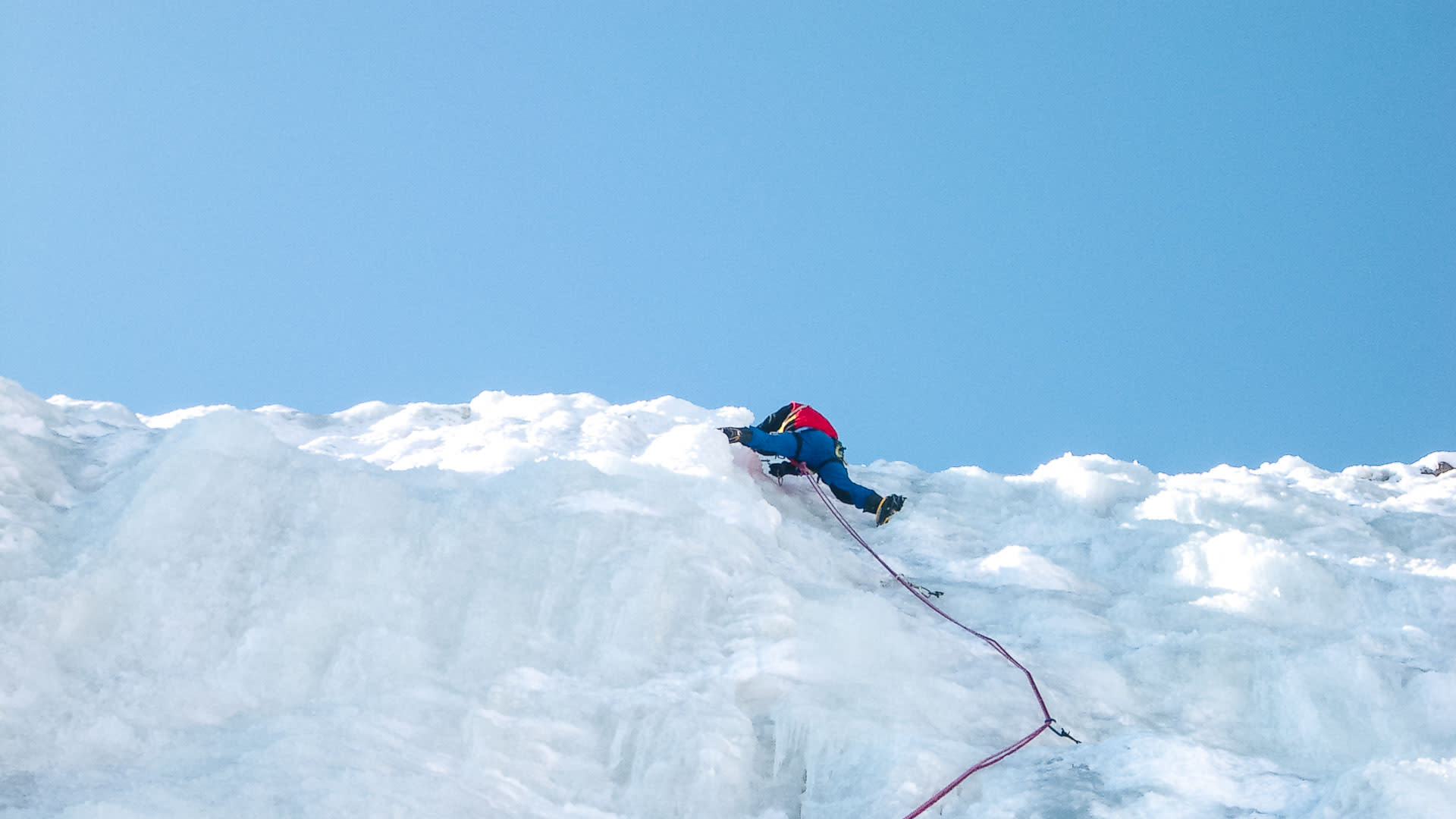 Eiskletterer in blauer Jacke steigt mit Pickeln und gelben Steigeisen eine senkrechte Eiswand in Mordor bei Bad Gastein auf.