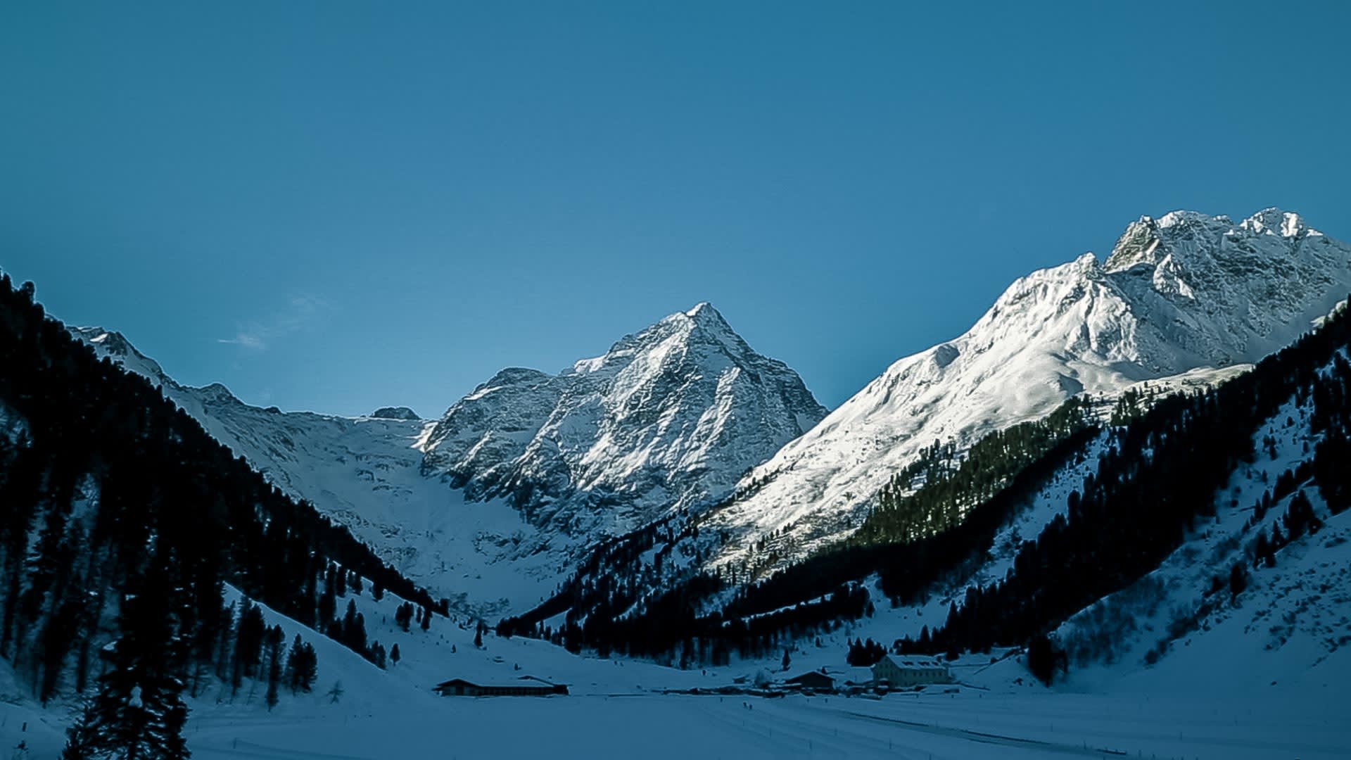 Eisklettern im Sellrain: Winterliches Tal bei Lüsens mit schneebedeckten Berggipfeln und Almhütten im Talgrund.