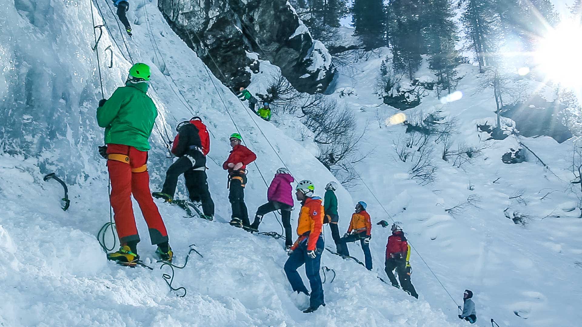 Eisklettern Training an gefrorenem Wasserfall: Gruppe mit Helmen, Steigeisen und Toprope-Seilen übt Eiskletter-Technik im Winter
