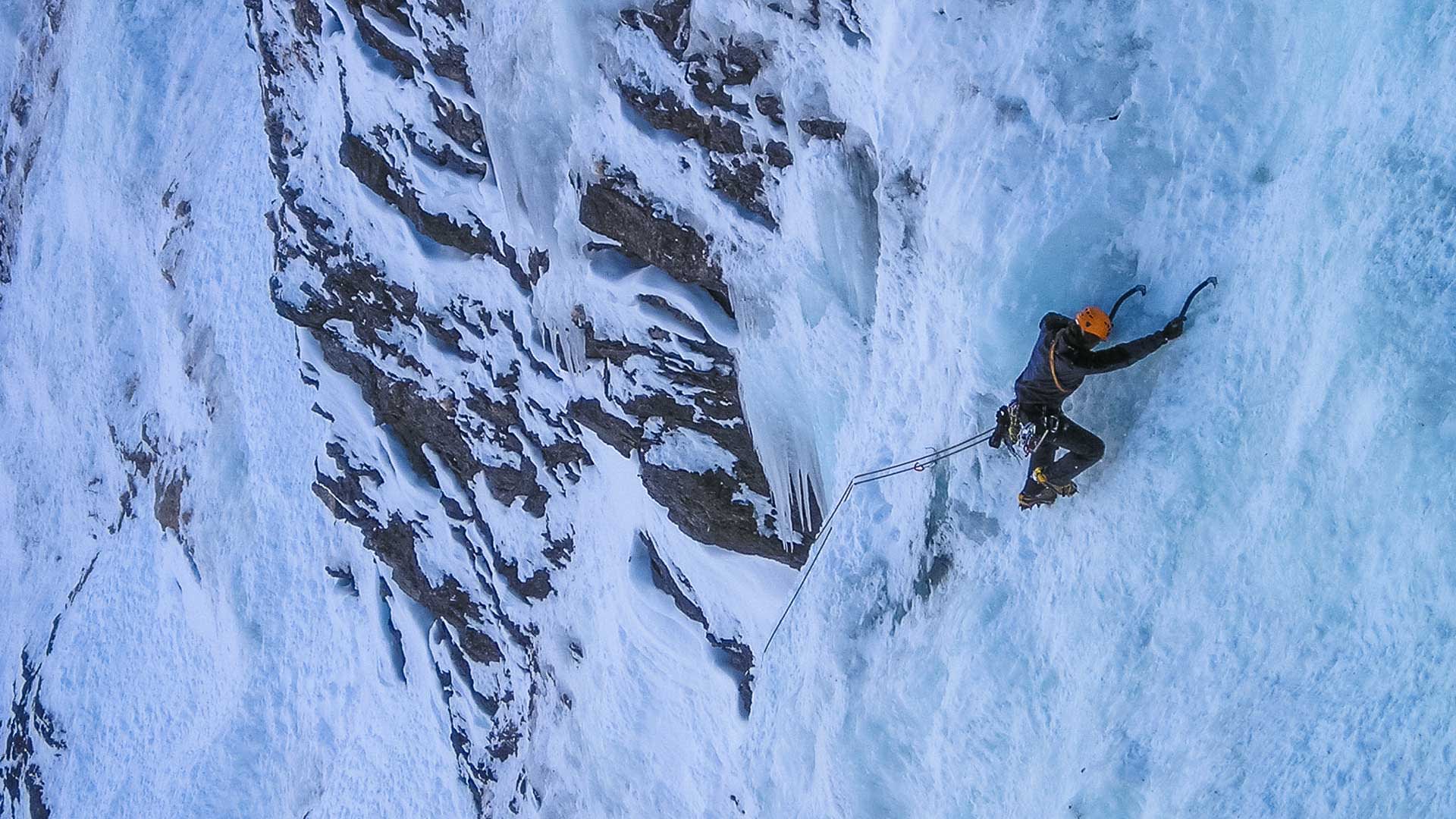 Eiskletterer mit Helm, Steigeisen und Eisäxten steigt in Vogelperspektive eine Eiswand in Bad Gastein hoch.
