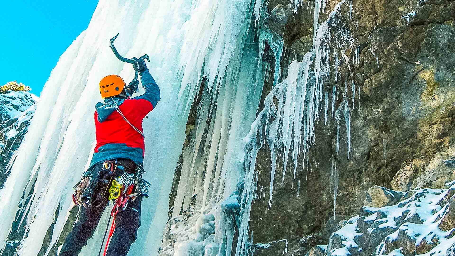 Eiskletterer schlägt mit zwei Eispickeln in eine senkrechte Eiswand an einem gefrorenen Wasserfall in den Dolomiten.