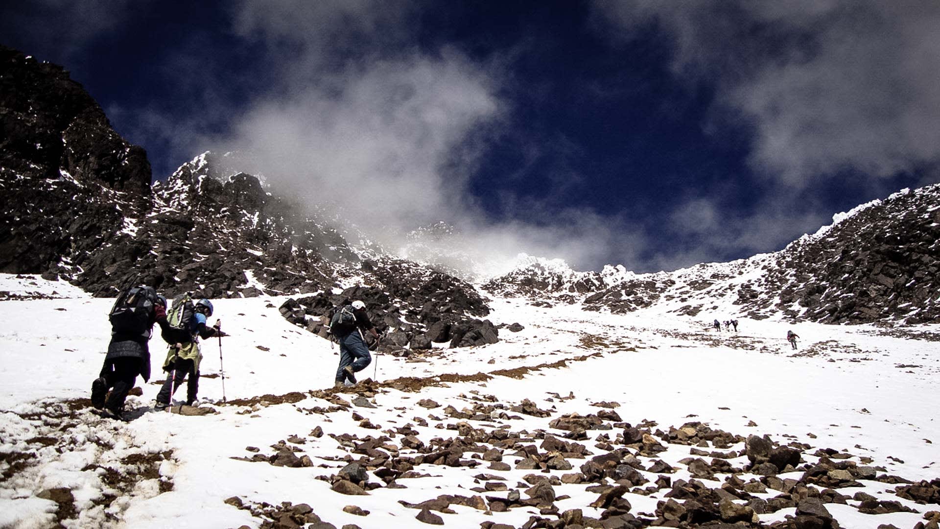 Expedition zum Illiniza Norte: sieben Höhenbergsteiger steigen über schneebedecktes Kar mit Geröll auf.