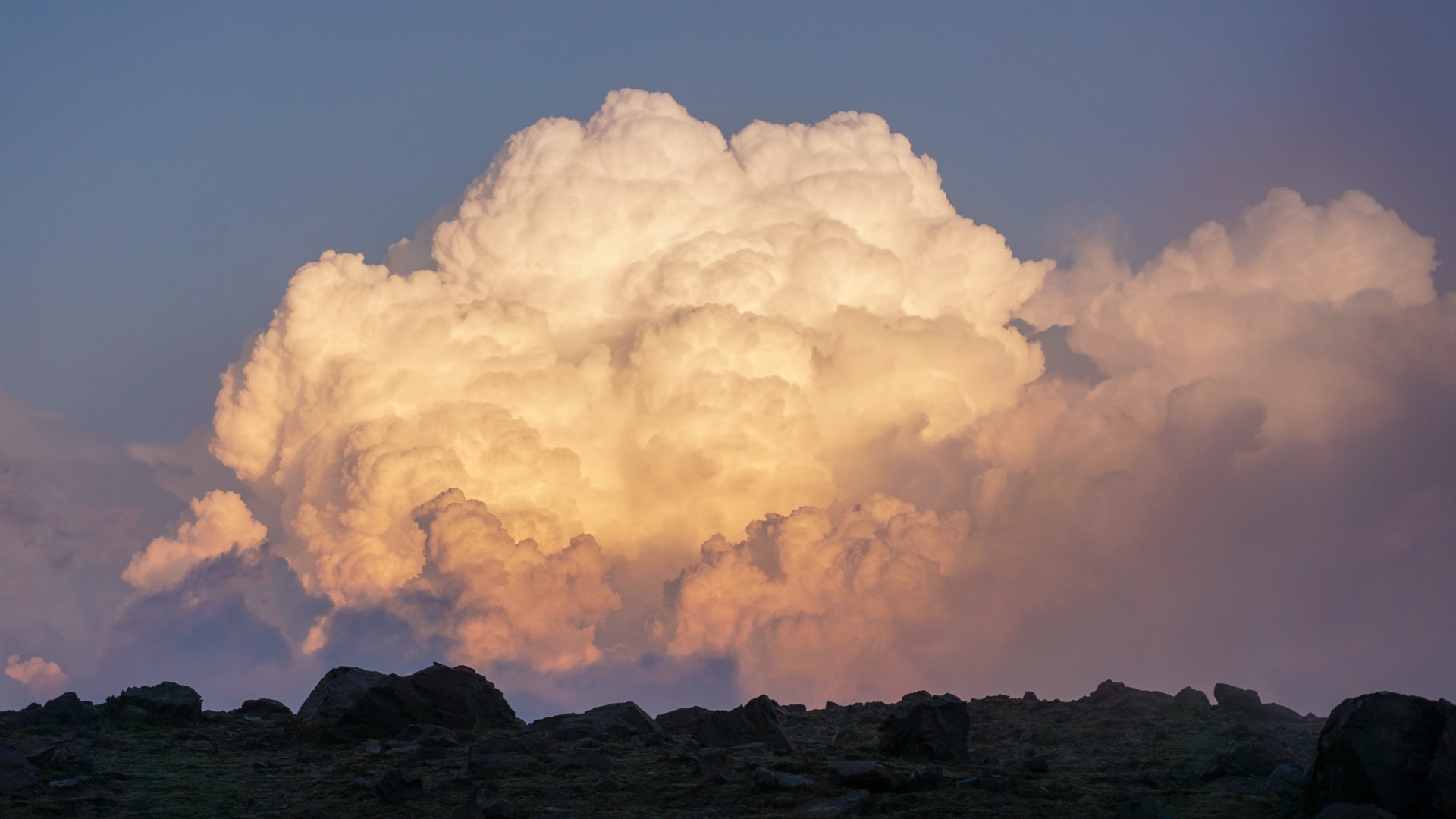 Expedition in den Anden: mächtiger Cumulonimbus-Wolkenturm im Abend- oder Morgenlicht über dunkler Felssilhouette.