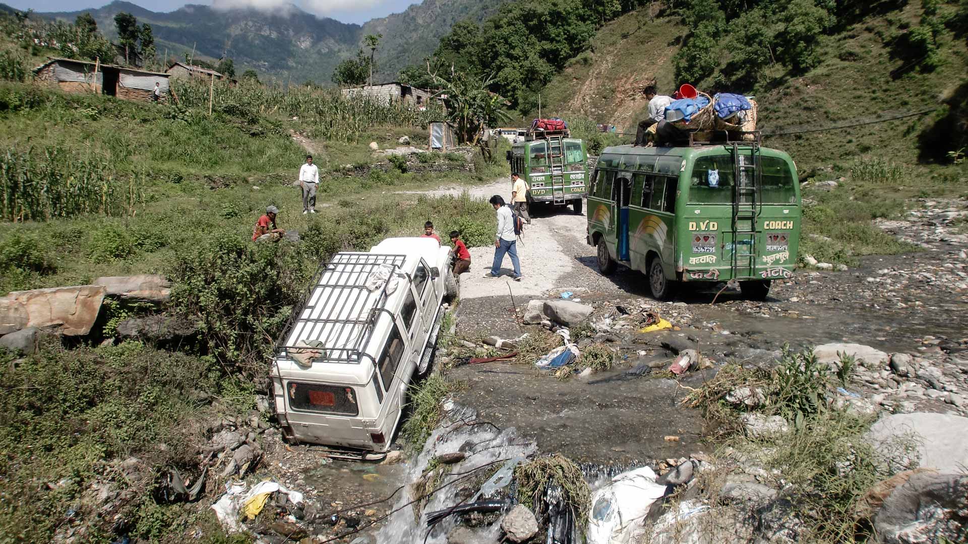 Himlung Himal Expedition: Fahrzeugwechsel in Besisahar – abgerutschter Kleinbus im Bach, grüne Überlandbusse und mehrere Personen