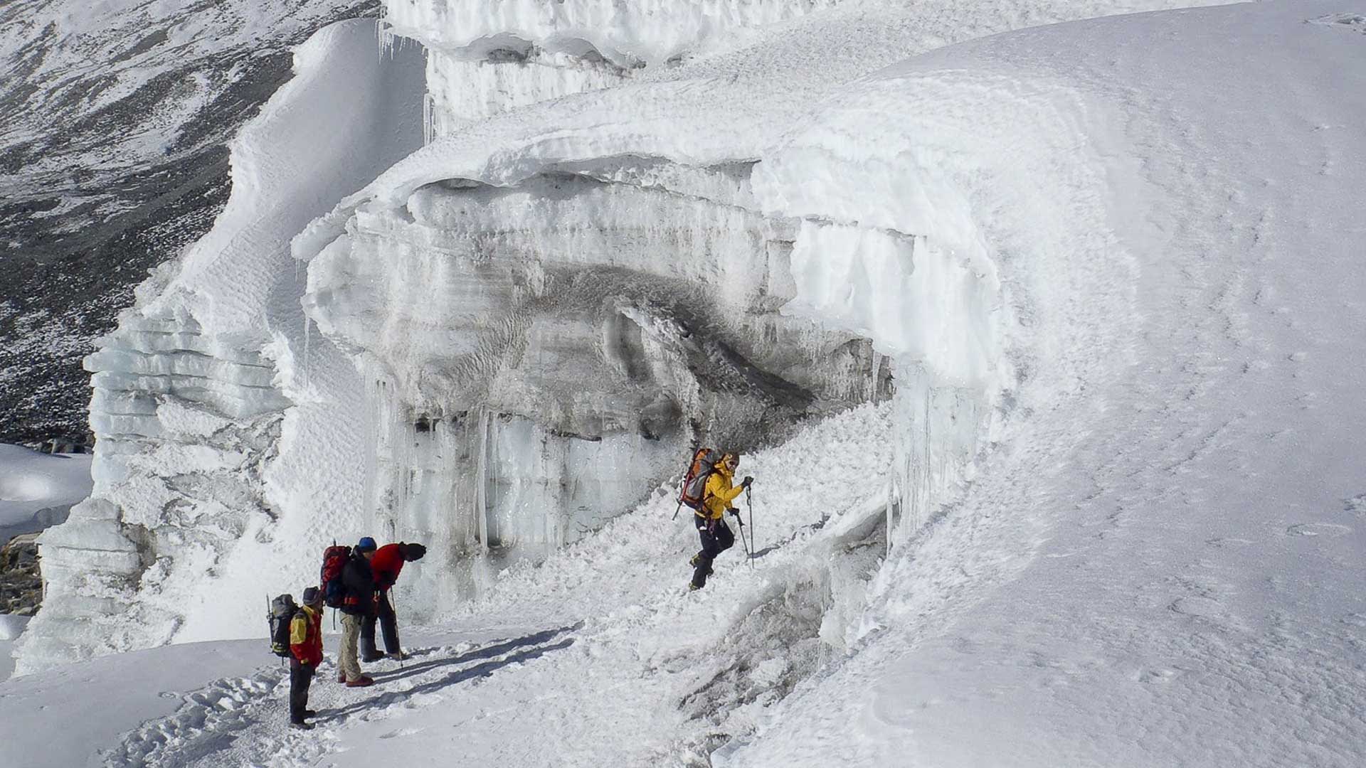Vier Höhenbergsteiger traversieren bläulich schimmernde Seracs und Eistrümmer am Amphu-Lapsa-Pass in Nepal.