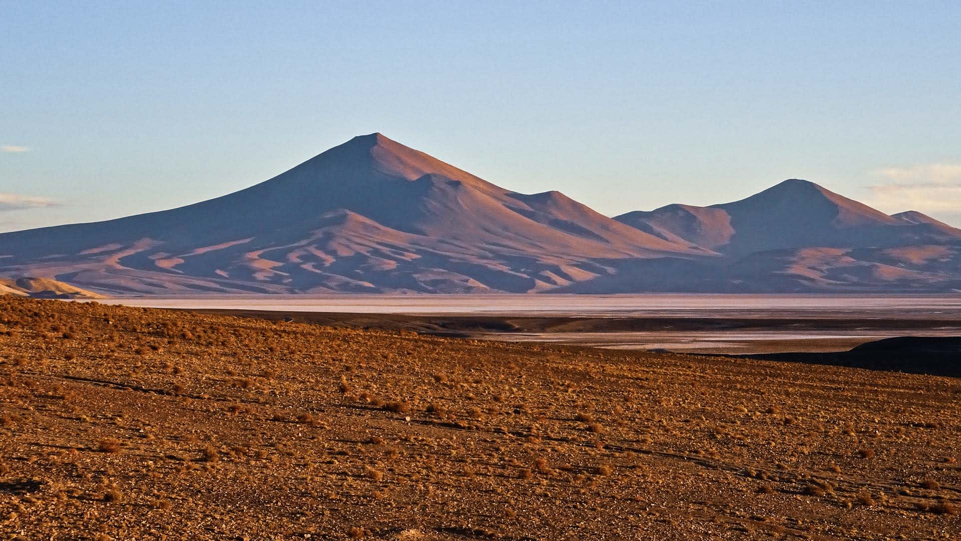 Expedition in der Atacama-Wüste: Salarsee-Band vor einem kegelförmigen Bergzug im Morgenlicht.