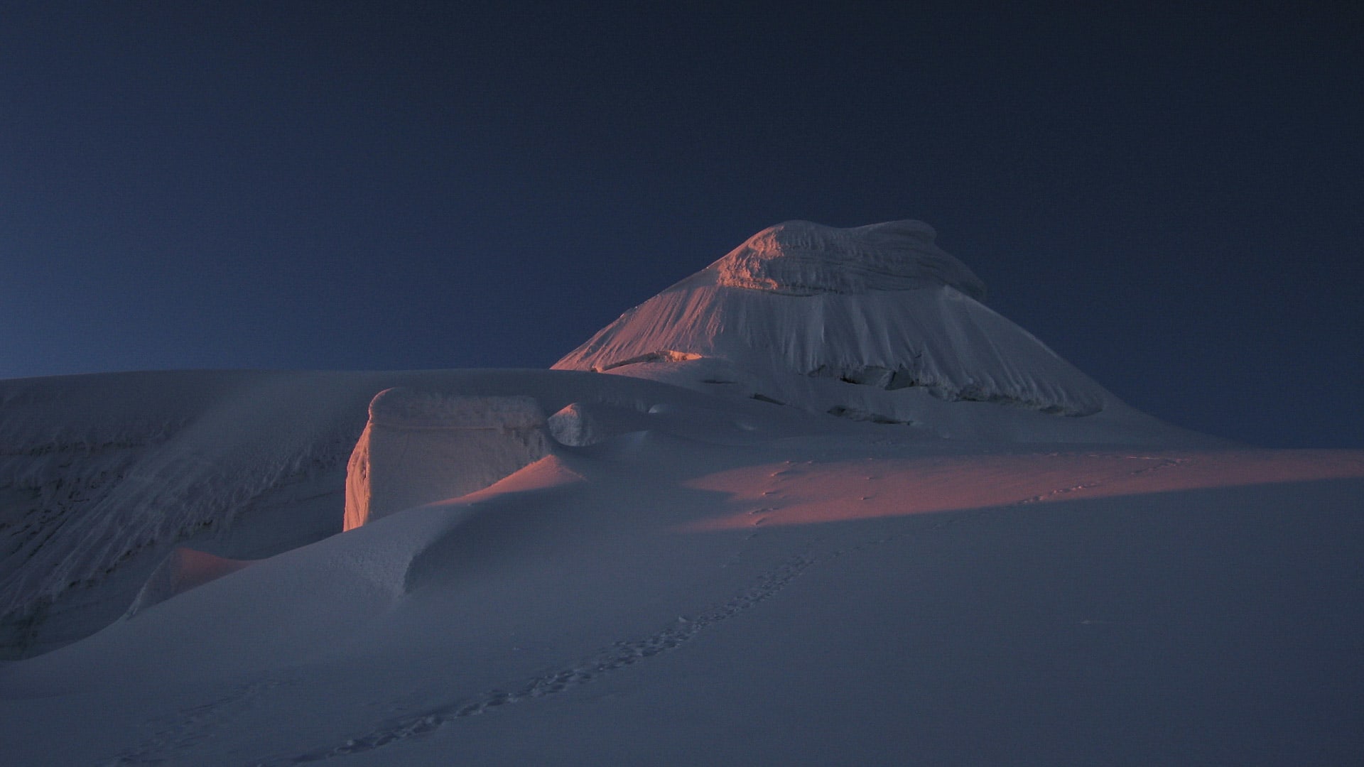 Expedition am Alpamayo: pyramidenförmiger Gipfel bei Morgenröte mit Fußspur im Firn und tiefblauem Himmel.