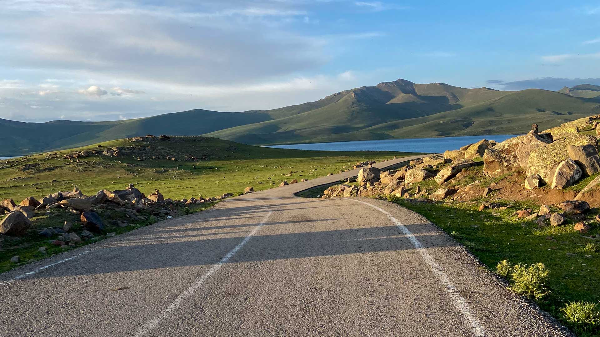 Schmale Asphaltstraße durch grüne Hochebene mit See und Hügeln beim Ararat-Trekking in der Türkei.