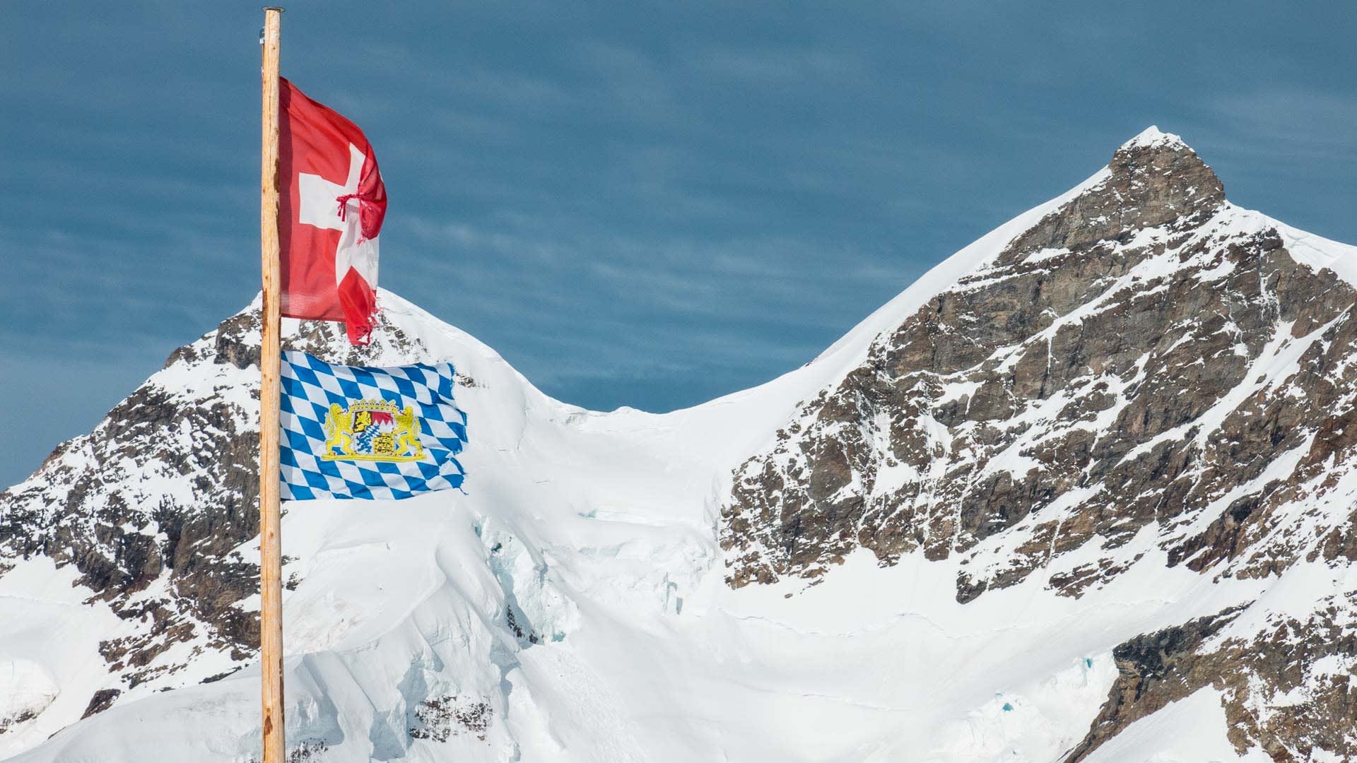 Hochtour im Berner Oberland bei Grindelwald: Schweizer Fahne und bayerische Flagge an Holzmast vor zwei stark schneebedeckten
