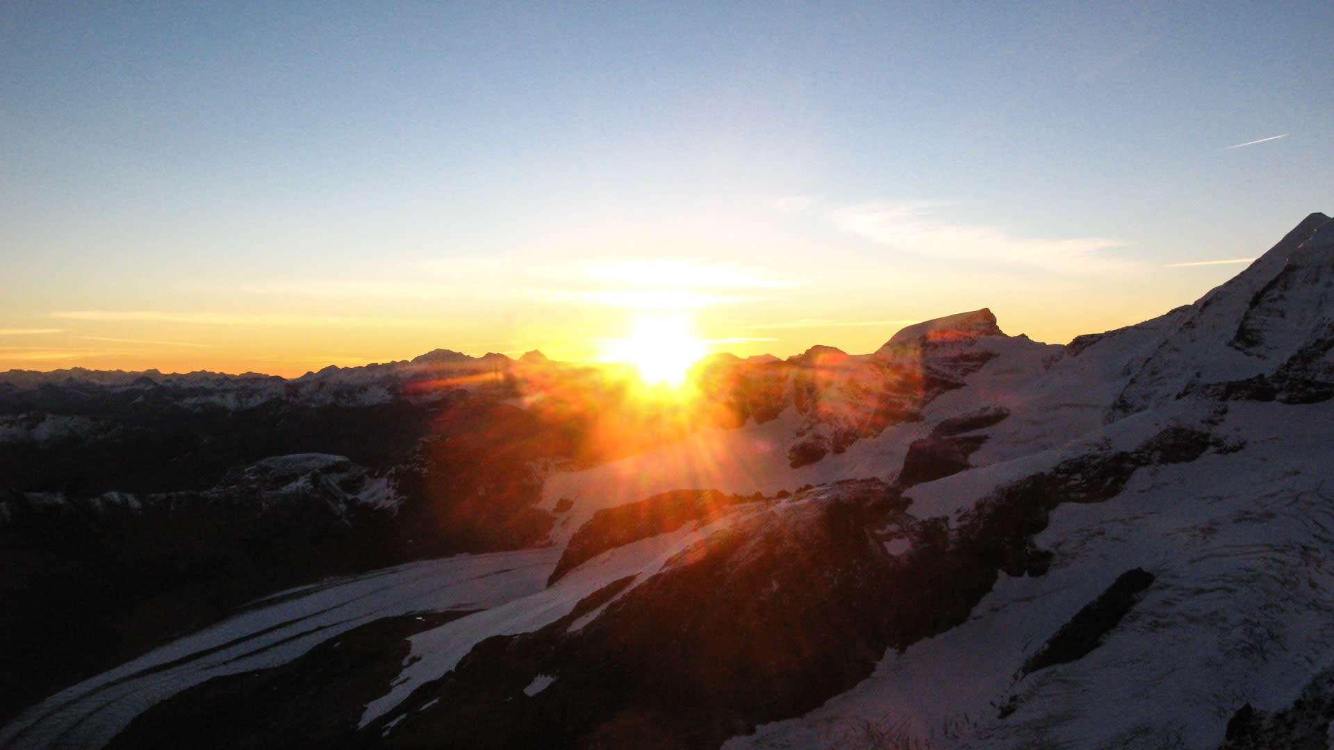 Hochtour in den Bernina-Alpen: schneebedeckte Gipfel und Hänge im Gegenlicht der tief stehenden Sonne mit sternförmigem Lensflare