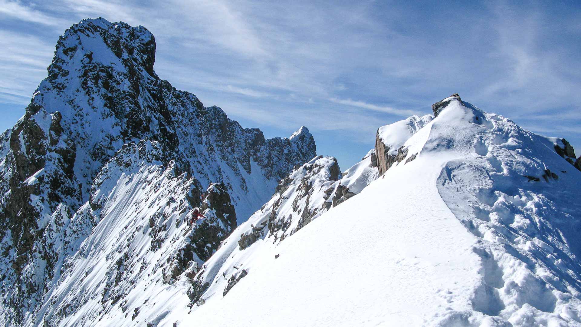 Hochtour am Biancograt: Bergsteiger in roter Jacke traversiert den verschneiten Grat unterhalb des Piz Bernina.
